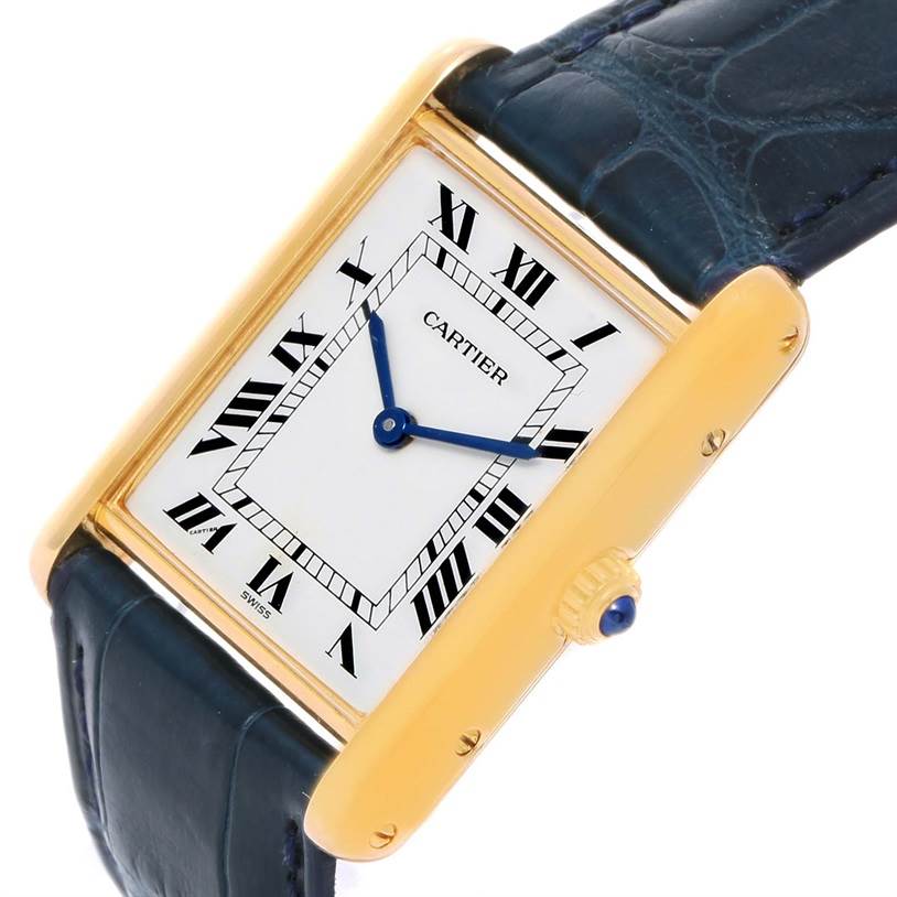 The Cartier Tank Classic Men's Yellow Gold White Dial Men's Yellow Gold White Dial watch is shown at an angle highlighting its face, blue hands, Roman numerals, and a textured blue strap.