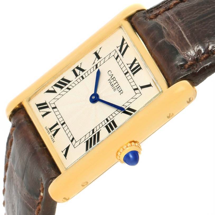 The Cartier Tank Classic Yellow Gold Silver Dial Yellow Gold Silver Dial watch is shown from a slightly tilted top-down angle, highlighting its face, brown leather strap, gold case, and blue crown.