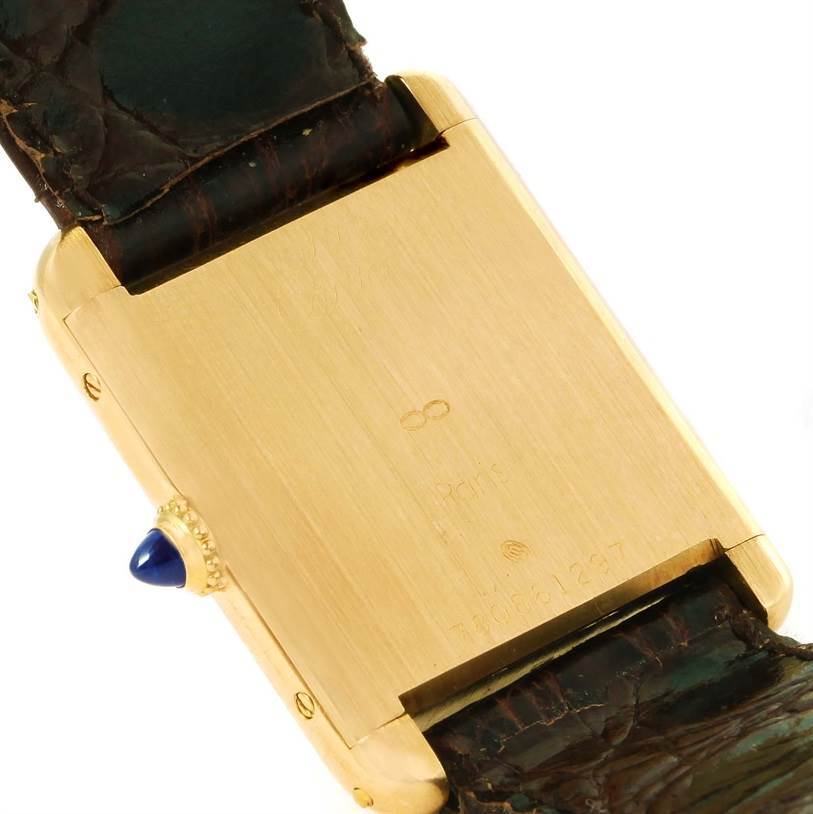 The image shows the back of a Cartier Tank Classic Men
s Yellow Gold White Dial Men
s Yellow Gold White Dial watch, highlighting its gold case and dark leather strap.