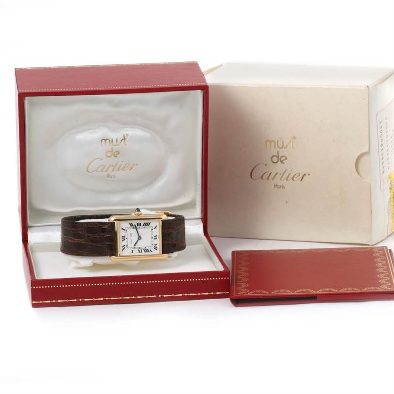 The Cartier Tank Classic Men
s Yellow Gold White Dial Men
s Yellow Gold White Dial watch is shown front-facing in its red box, along with its outer box and booklet.