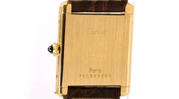This image shows the back of a Cartier Tank Classic Men's Yellow Gold White Dial Men's Yellow Gold White Dial watch, highlighting the brand engraving and serial number.