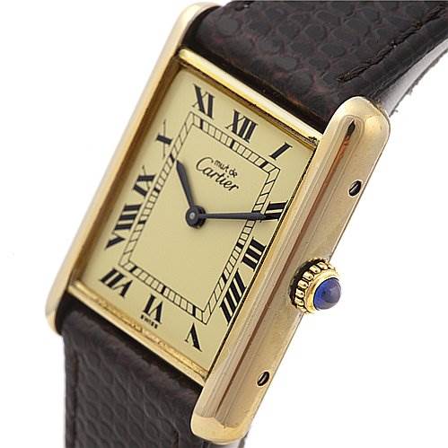 The image shows a close-up of the Cartier Tank Classic Yellow Gold Beige Dial Yellow Gold Beige Dial watch, displaying the face, Roman numerals, and part of the brown leather strap.