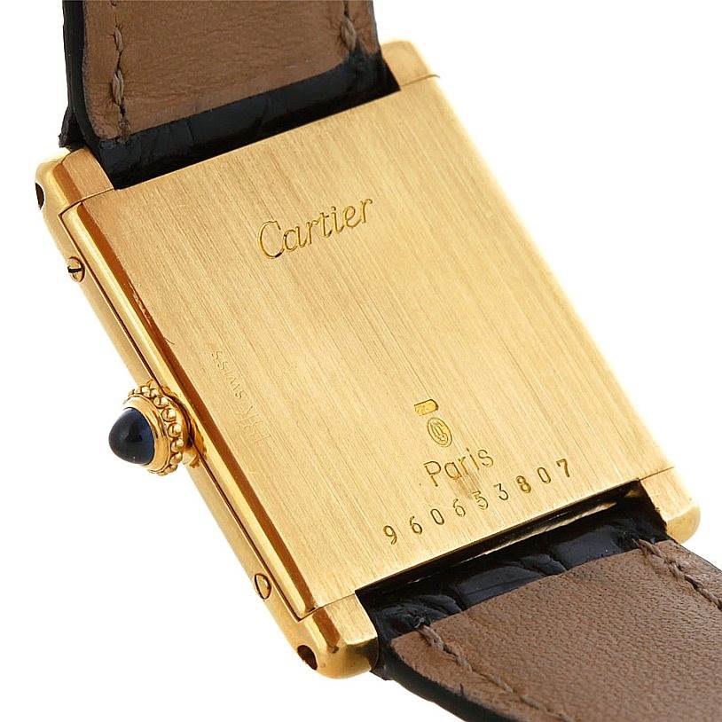 The image shows the back case and part of the leather strap of a Cartier Tank Classic Men's Yellow Gold White Dial Men's Yellow Gold White Dial watch.