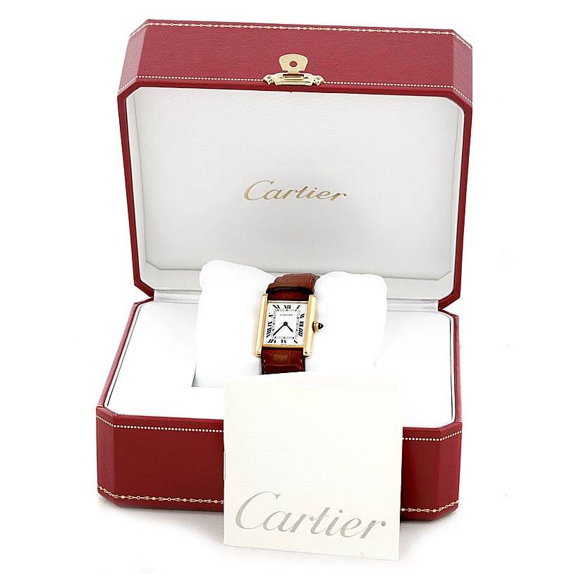 The Cartier Tank Classic Men
s Yellow Gold White Dial Men
s Yellow Gold White Dial watch is shown in its box, featuring the face and brown strap, with a Cartier booklet in front.