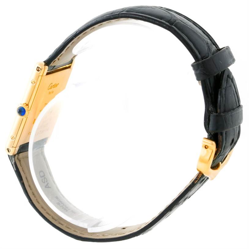 The image shows a side profile of the Cartier Tank Classic Men's Yellow Gold Beige Dial Men's Yellow Gold Beige Dial watch, highlighting the gold case, blue crown, and black leather strap with a buckle.