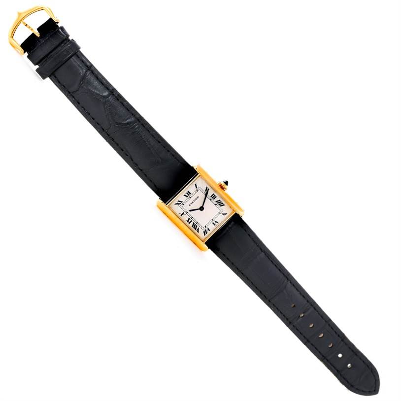 The image shows a top view of a Cartier Tank Classic Men's Yellow Gold Beige Dial Men's Yellow Gold Beige Dial watch, highlighting its square face, black leather strap, and gold casing.