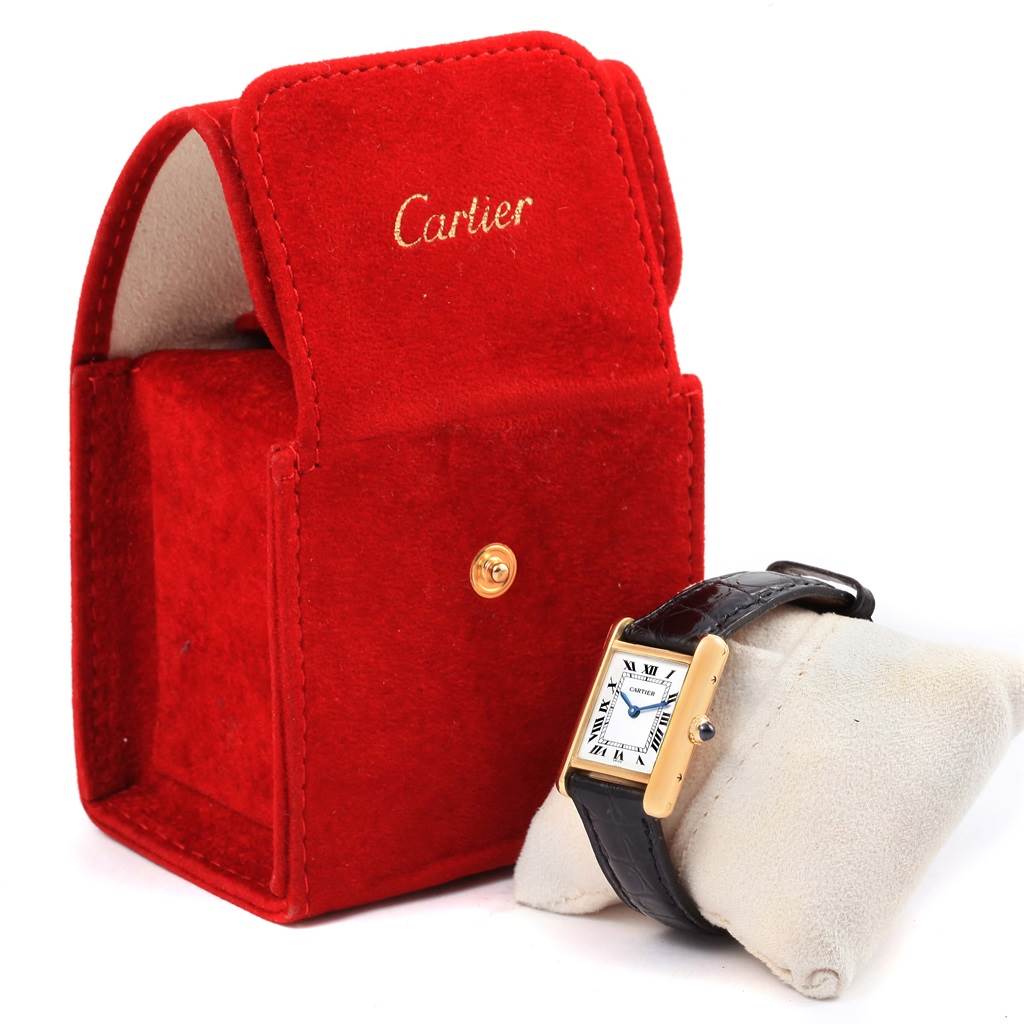 The image shows a Cartier Tank Classic Women's Yellow Gold White Dial Women's Yellow Gold White Dial watch on a cushion with a red Cartier case in the background.
