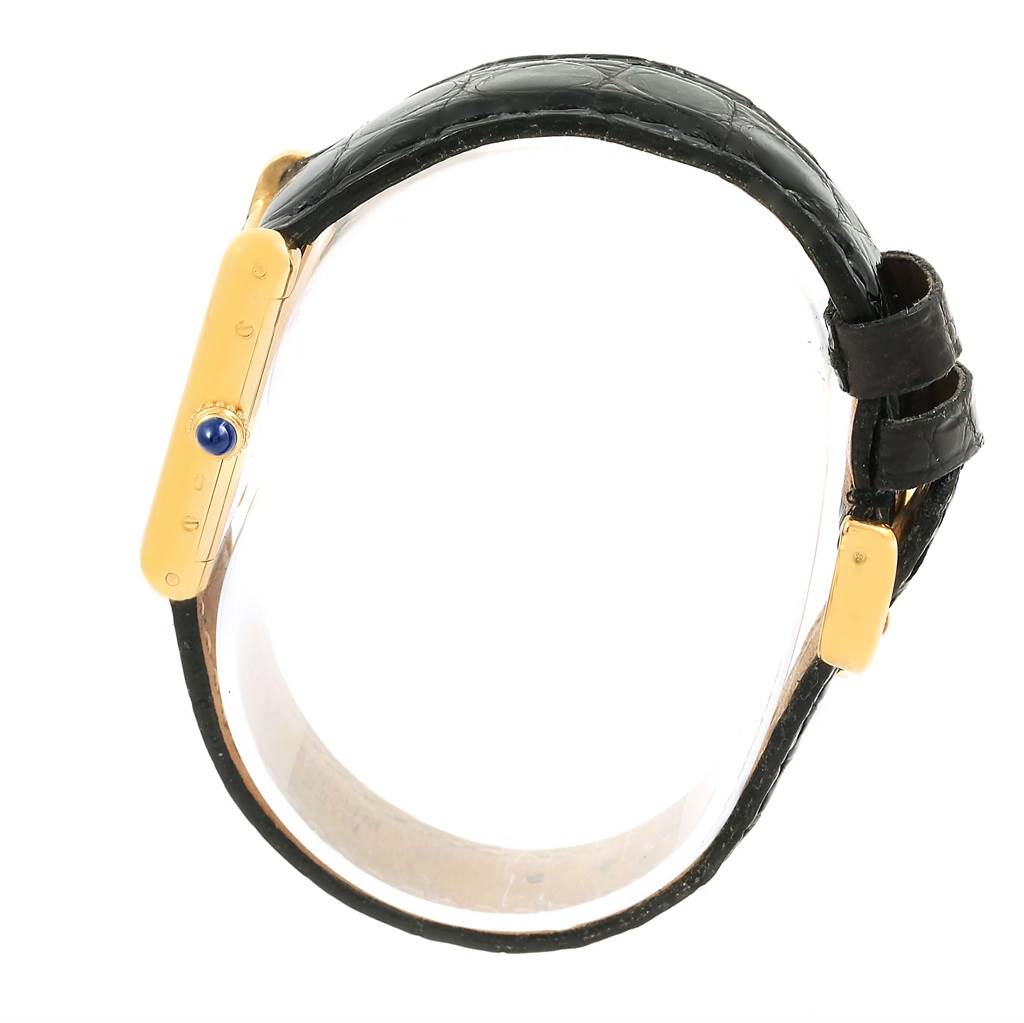 The image shows a Cartier Tank Classic Women's Yellow Gold White Dial Women's Yellow Gold White Dial watch in a side profile, highlighting its gold case, crown with blue stone, and black leather strap.