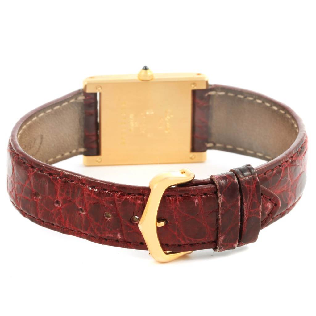 The image shows the back of a Cartier Tank Classic Women's Yellow Gold White Dial Women's Yellow Gold White Dial watch and its red leather strap with a gold buckle.