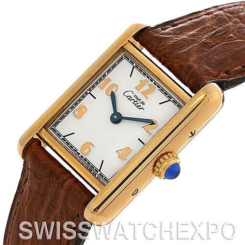 This image shows a Cartier Tank Classic Women's Yellow Gold White Dial Women's Yellow Gold White Dial watch, angled to highlight its face, gold bezel, brown leather strap, and blue cabochon crown.