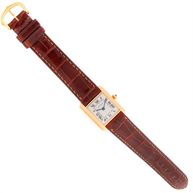 The image shows a top-down view of a Cartier Tank Classic Women's Yellow Gold Silver Dial Women's Yellow Gold Silver Dial watch with a gold case and a brown leather strap.