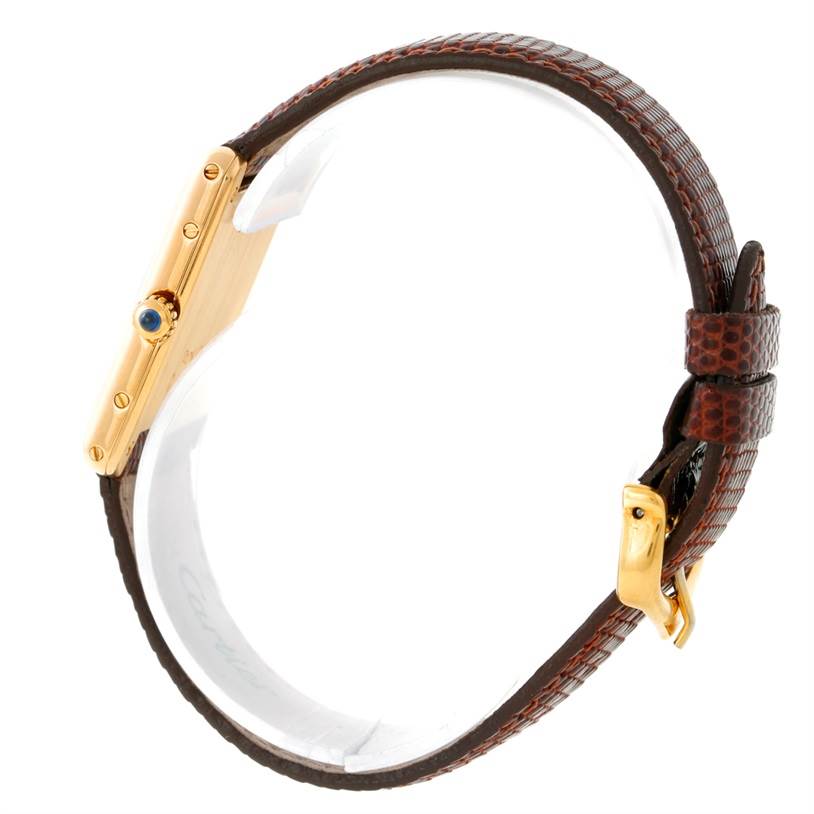 This image shows a side view of the Cartier Tank Classic Yellow Gold Beige Dial Yellow Gold Beige Dial watch, highlighting the gold case, crown with a blue gemstone, and brown leather strap.