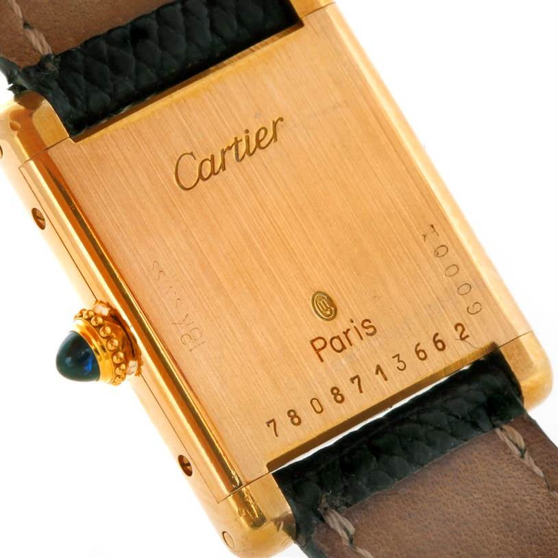 This image shows the back of a Cartier Tank Classic Women's Yellow Gold White Dial Women's Yellow Gold White Dial watch, displaying its gold case, serial number, and leather strap.