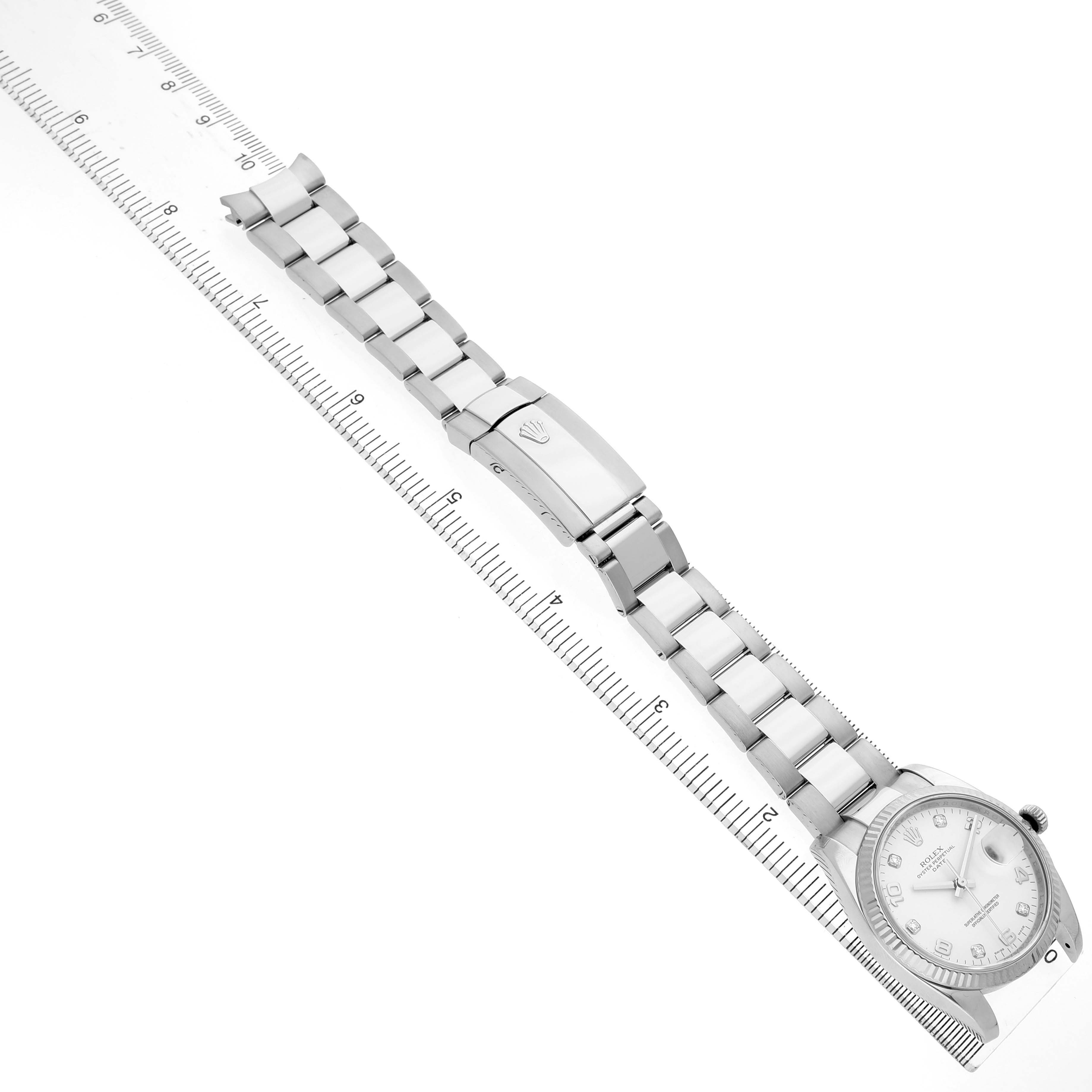 The Rolex Datejust 115234 Men's Stainless Steel White Dial watch is shown from a top-down angle, featuring the full bracelet, clasp, and watch face alongside a measuring ruler.
