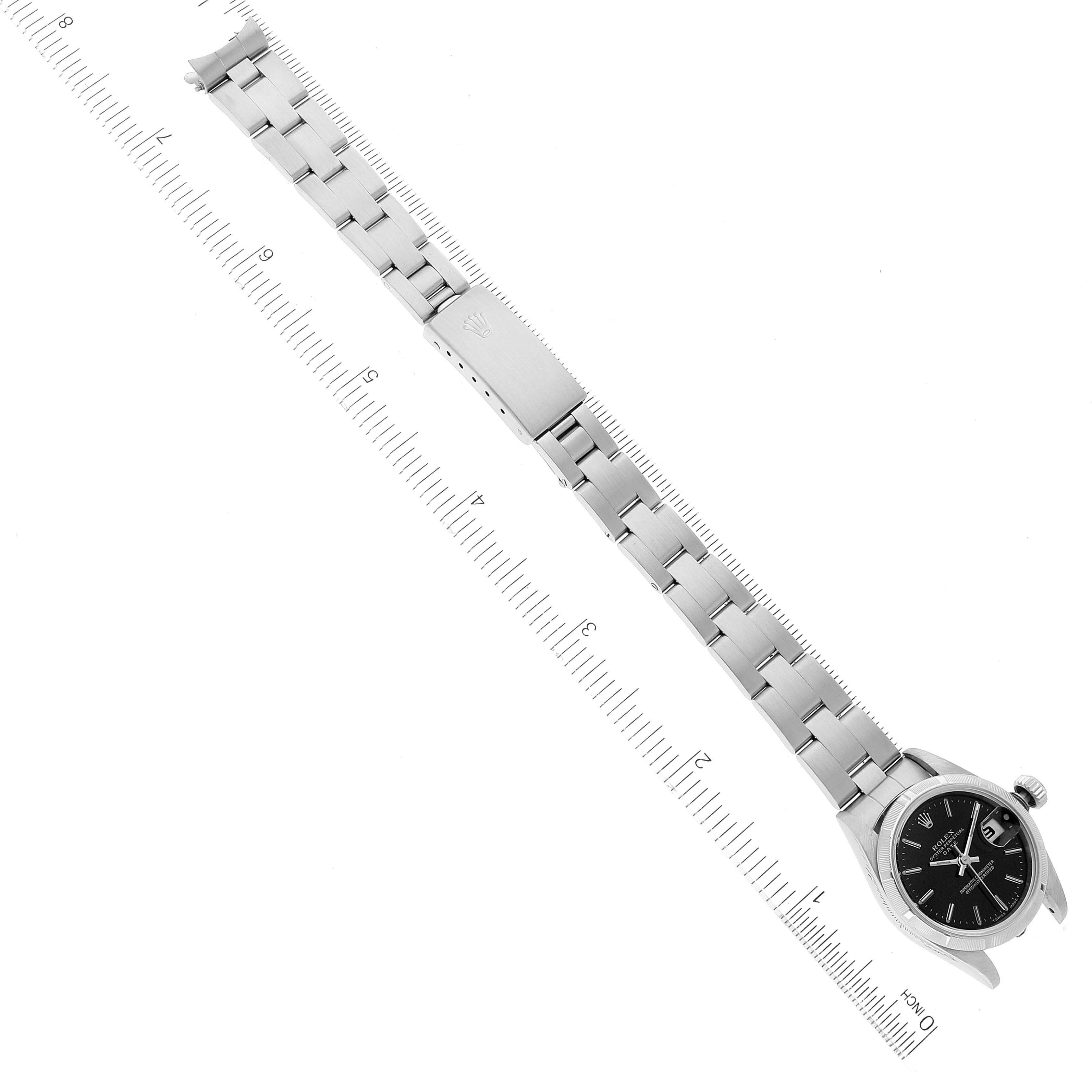 The image shows a top-down view of a Rolex Date 69190 Women
s Stainless Steel Black Dial 69190 Women
s Stainless Steel Black Dial model watch, displaying the watch face, band, and clasp alongside a measuring scale.