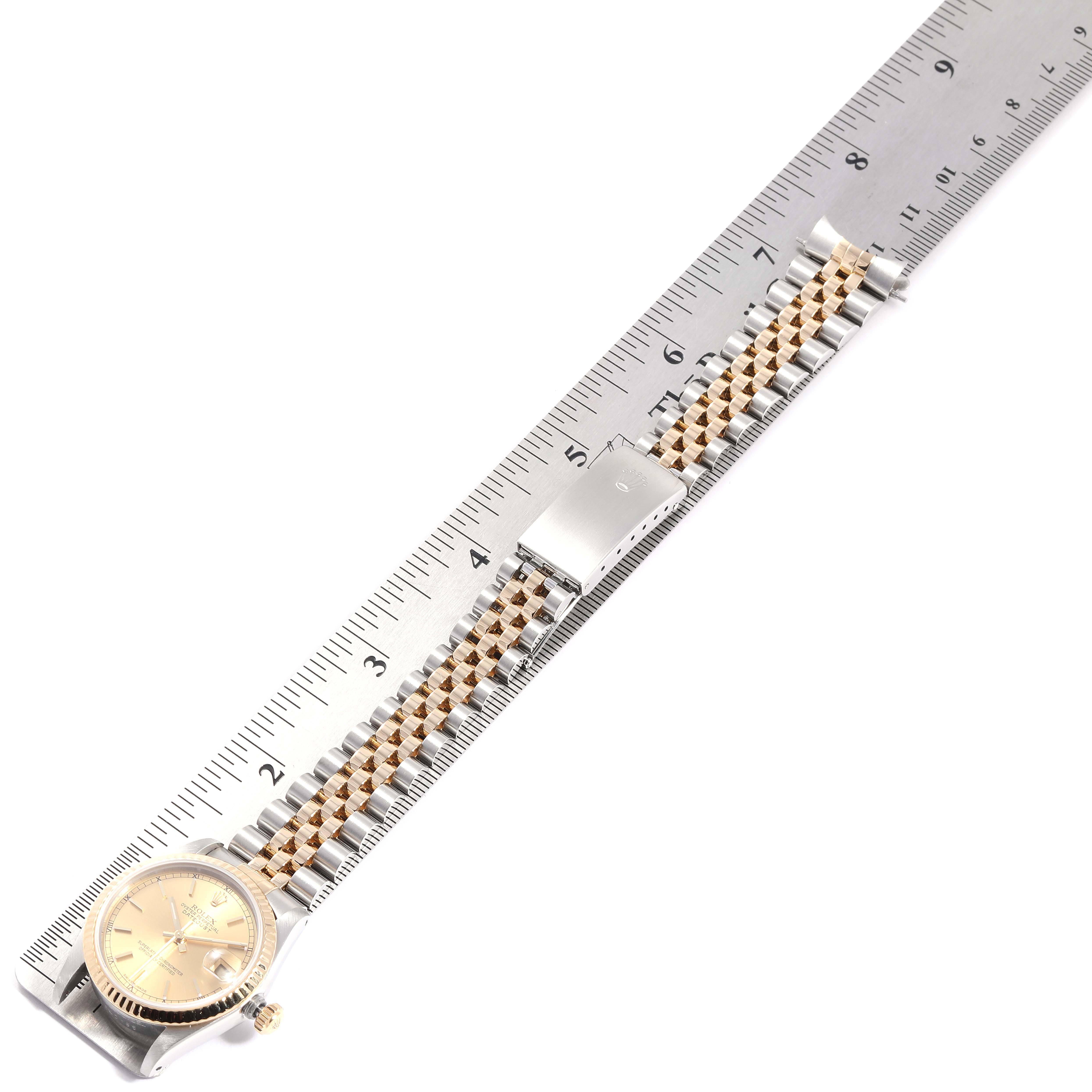 The image shows a Rolex Datejust 68273  Women
s Steel and Gold (two tone) Champagne Dial 68273  Women
s Steel and Gold (two tone) Champagne Dial watch laid flat on a ruler, displaying its face, strap, and clasp.