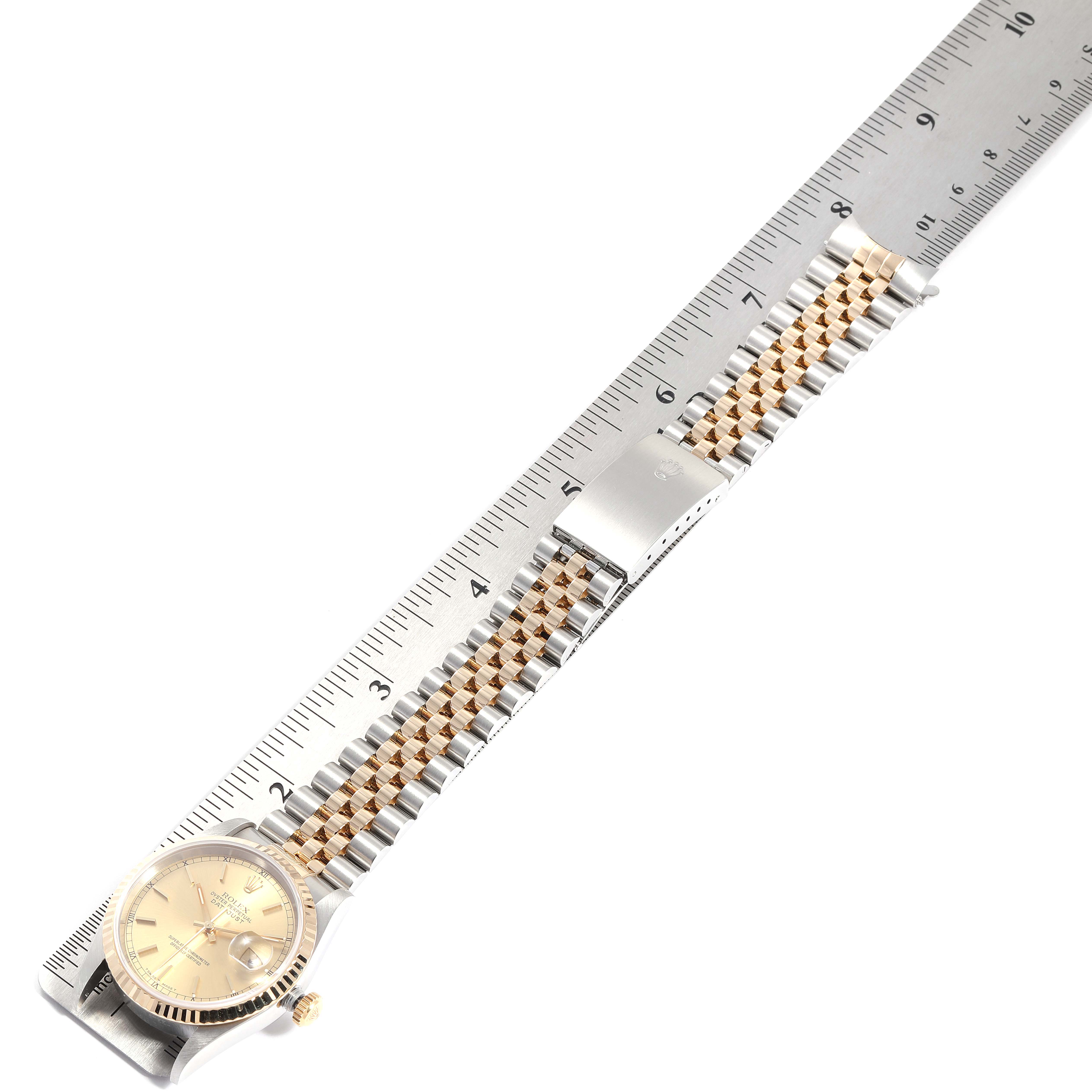 The image shows a Rolex Datejust 16233 Men
s Steel and Gold (two tone) Champagne Dial 16233 Men
s Steel and Gold (two tone) Champagne Dial watch placed next to a ruler, highlighting its face, bracelet, and clasp.
