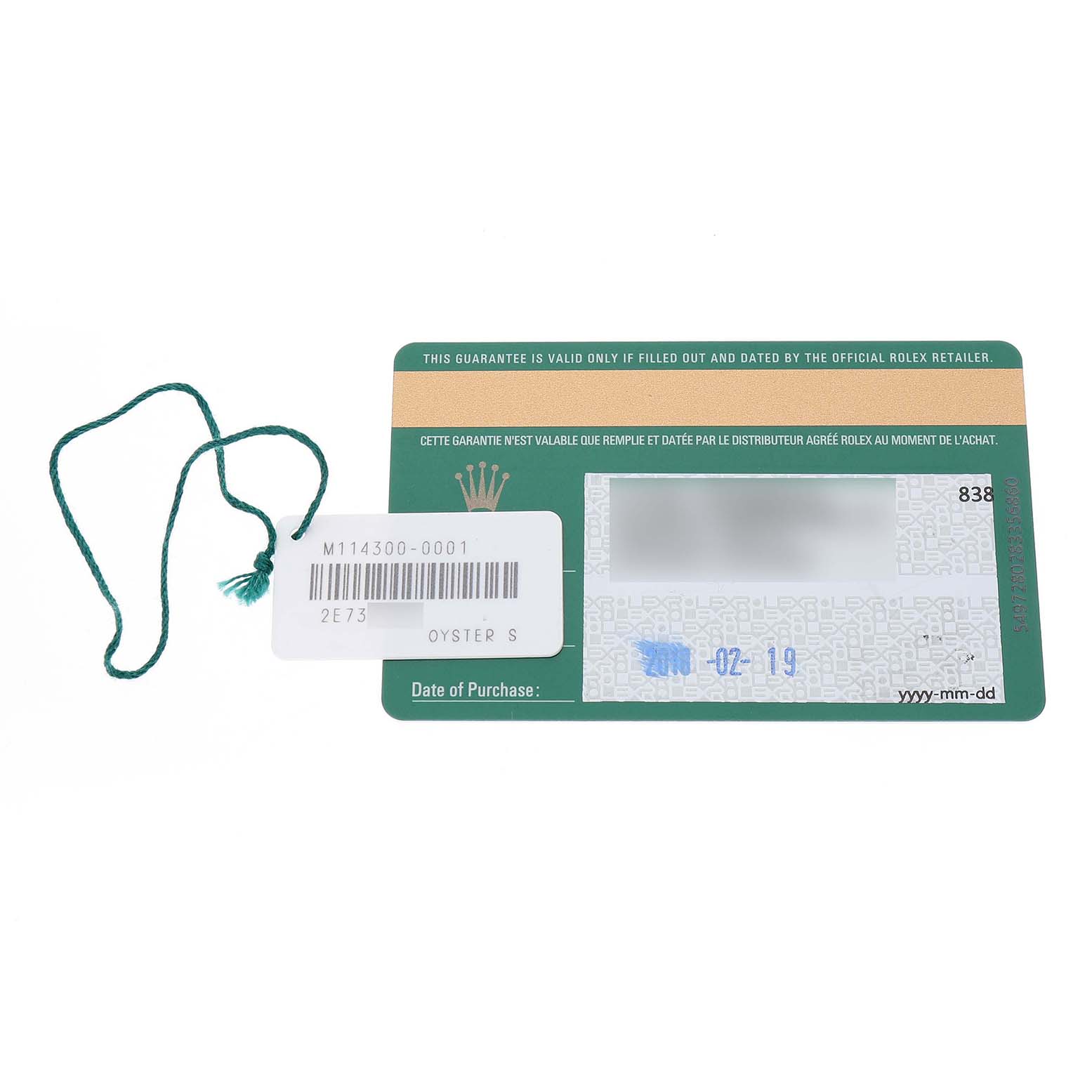 The image shows the warranty card and a green tag from a Rolex Oyster Perpetual 114300 Men's Stainless Steel Grey Dial watch, viewed from above.