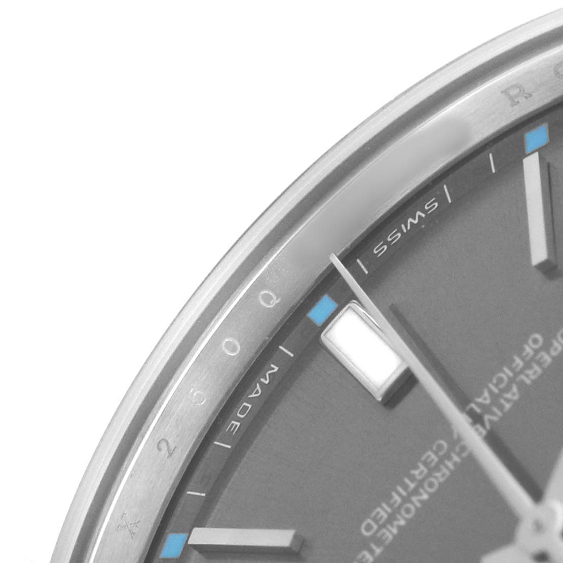 The image shows a close-up of the dial and bezel of a Rolex Oyster Perpetual 114300 Men's Stainless Steel Grey Dial watch, featuring partial hour markers and the word "SWISS."