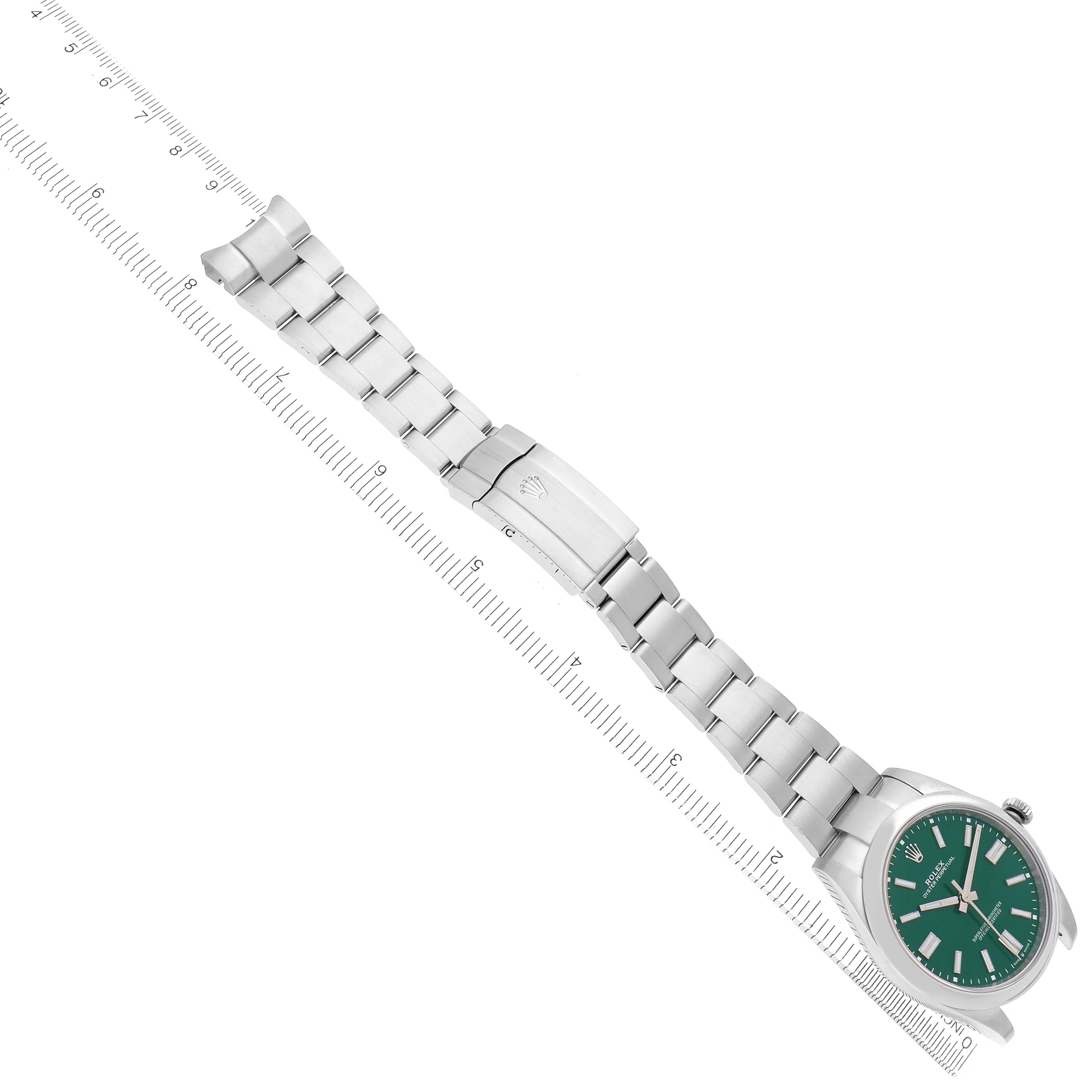 The Rolex Oyster Perpetual model 124300 is shown from an angled overhead view, highlighting its green dial, metal bracelet, and clasp in full extension.