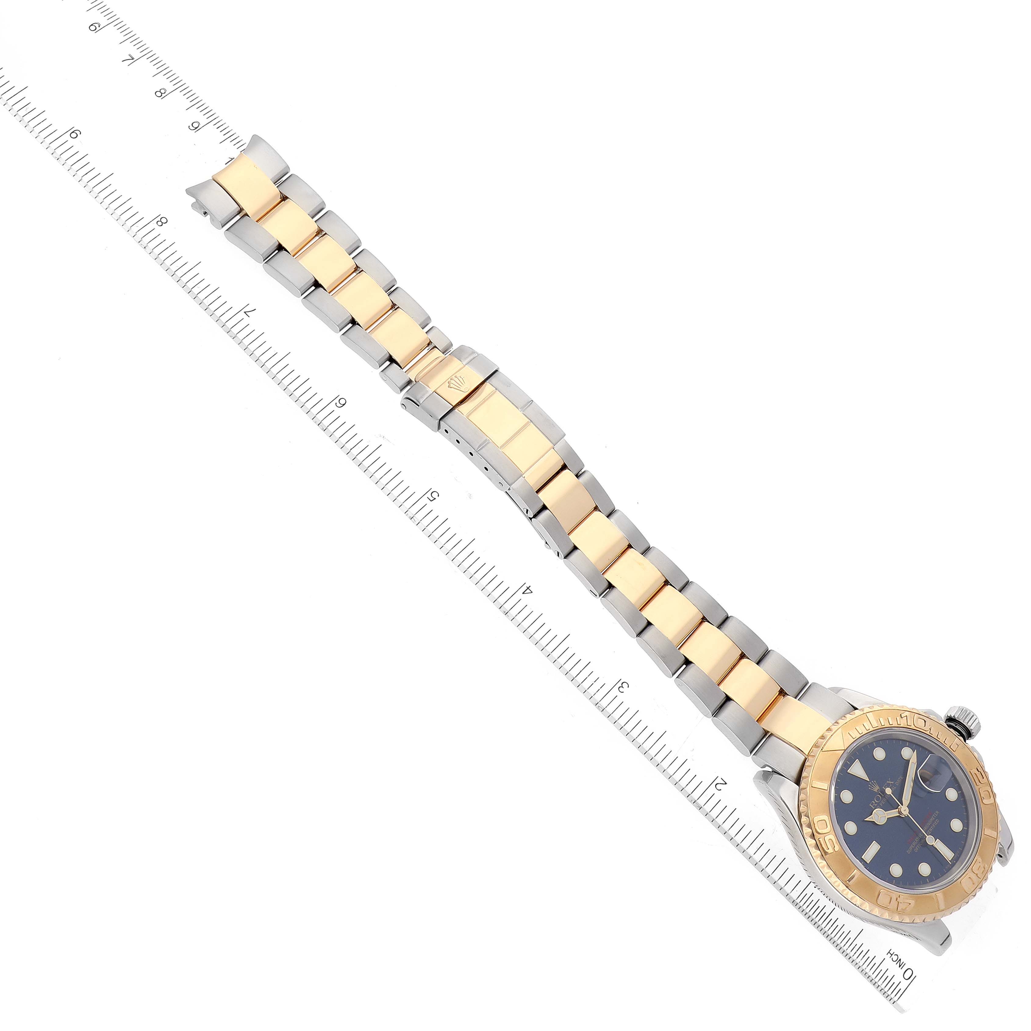 The image shows a Rolex Yacht-Master 16623 Men
s Steel and Gold (two tone) Blue Dial 16623 Men
s Steel and Gold (two tone) Blue Dial watch laid flat with its full bracelet visible, next to a measuring ruler for scale.