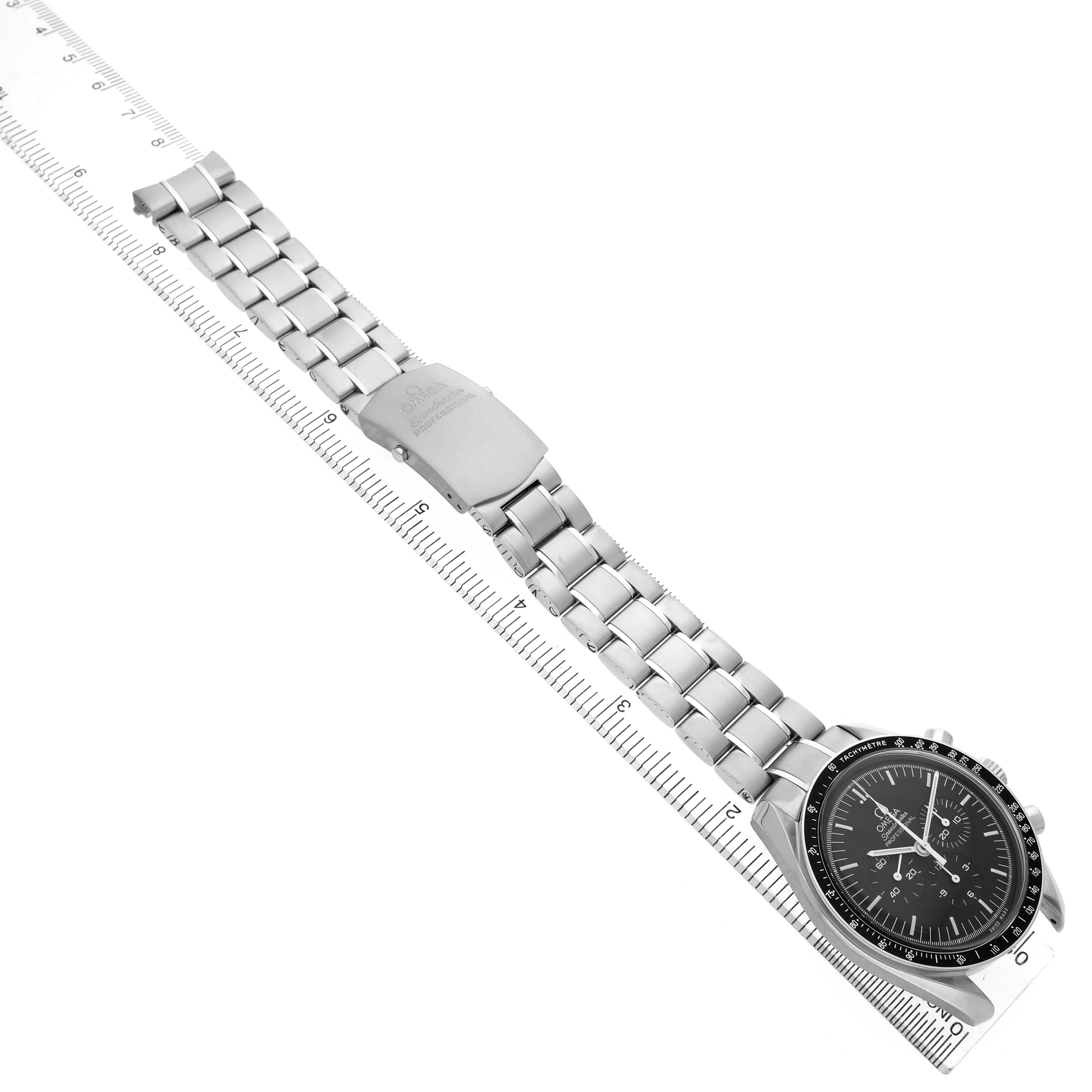 The Omega Speedmaster 311.30.42.30.01.005 Men's Stainless Steel Black Dial watch is angled diagonally, showing the complete bracelet, clasp, and face next to a ruler.