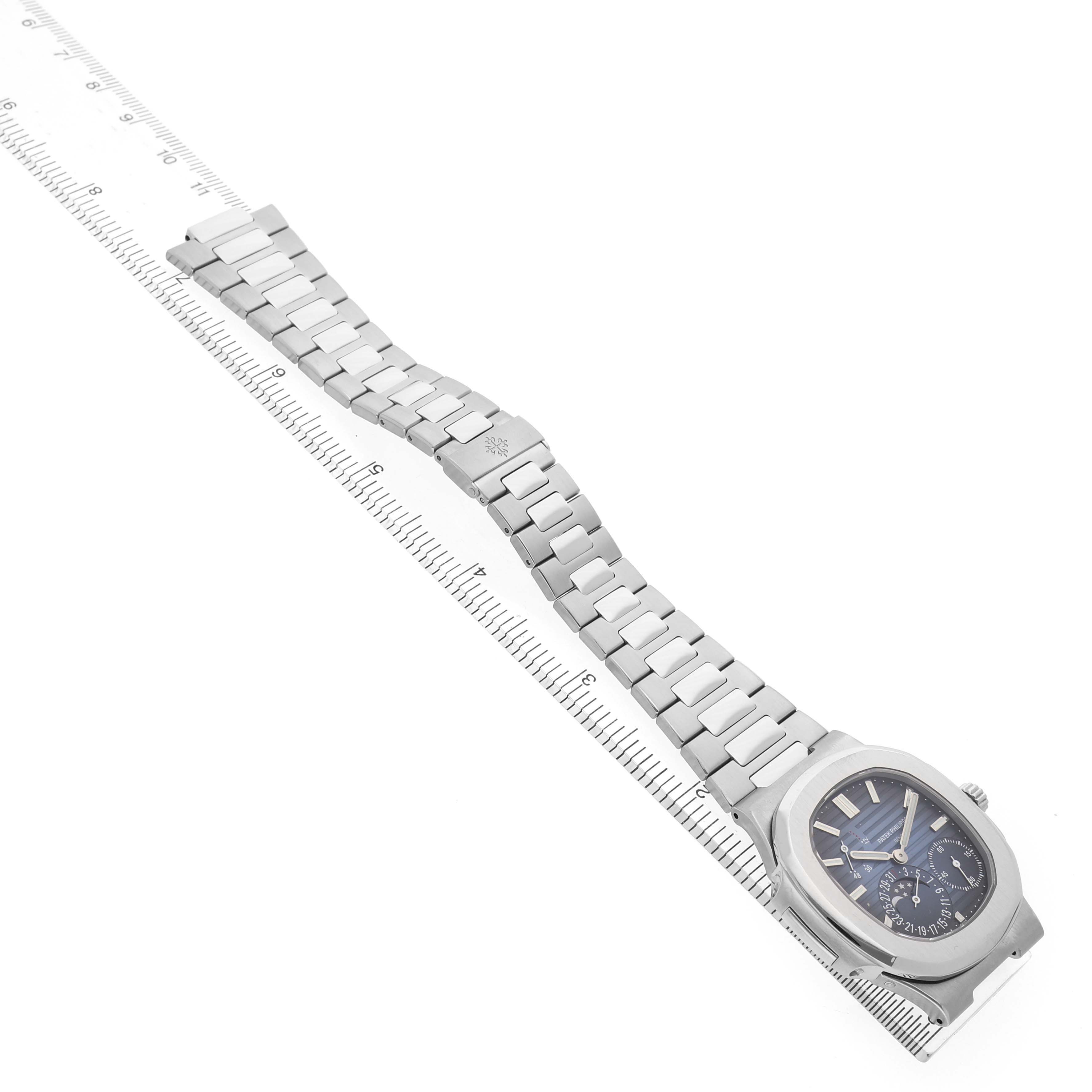 The image shows a Patek Philippe Nautilus 5712A Men's Stainless Steel Blue Dial watch displayed diagonally with its bracelet extended, alongside a measuring ruler.