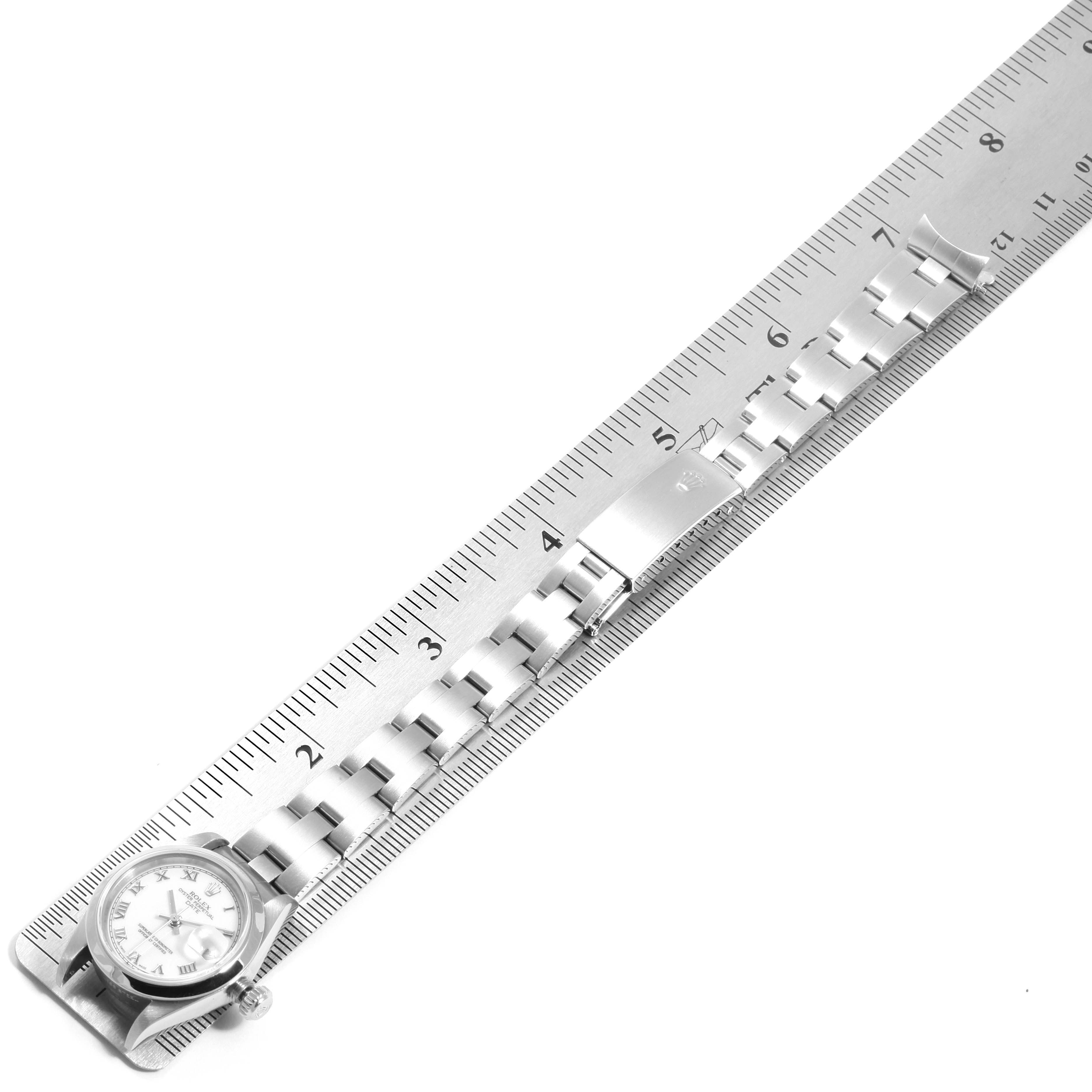The image shows a Rolex Date 79160  Women
s Stainless Steel White Dial 79160  Women
s Stainless Steel White Dial model watch laid flat against a ruler, depicting the watch case and stainless steel bracelet.