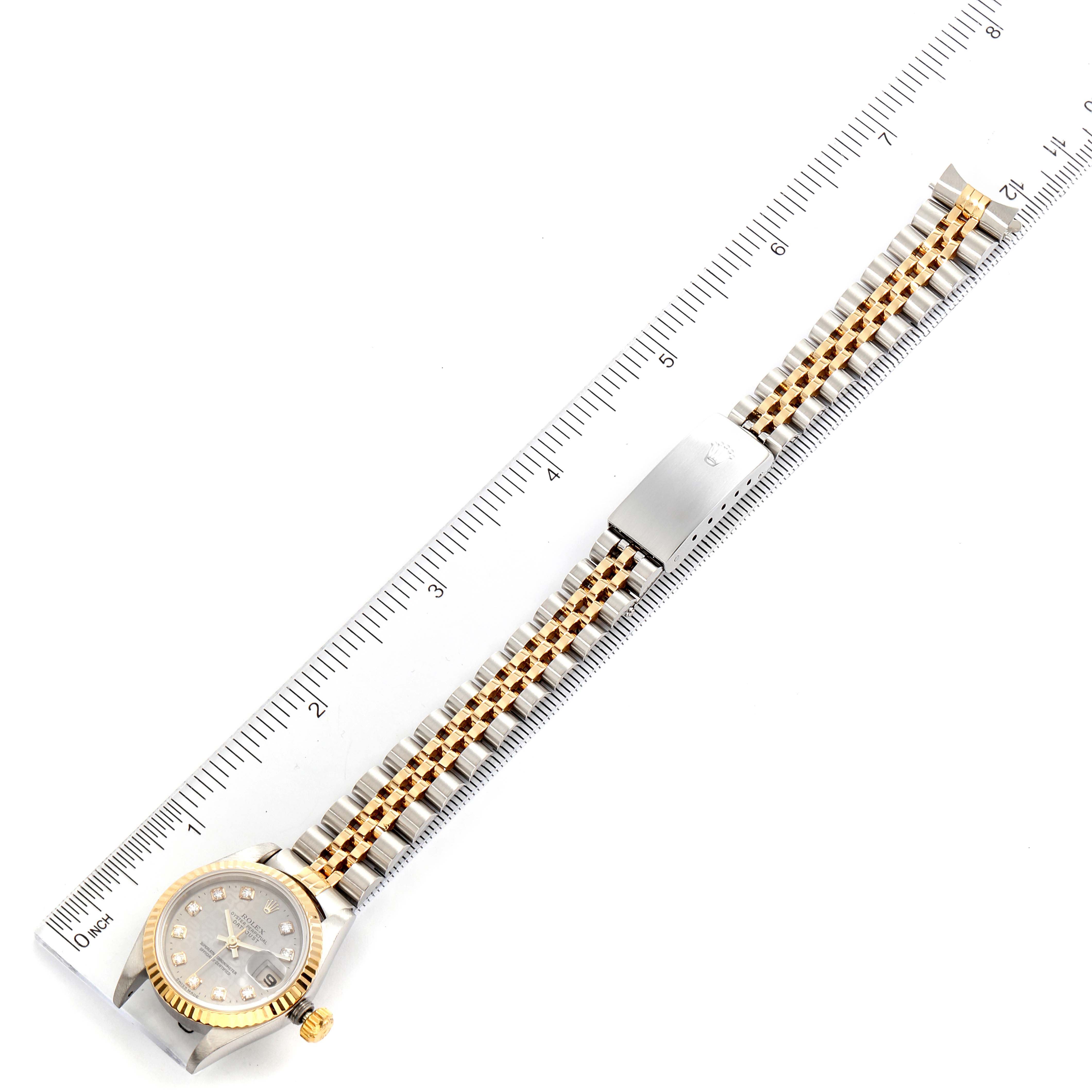 The image shows a top-down view of a Rolex Datejust 69173 Women
s Steel and Gold (two tone) Grey Dial 69173 Women
s Steel and Gold (two tone) Grey Dial watch with a ruler, displaying the watch face, bezel, crown, and bracelet.