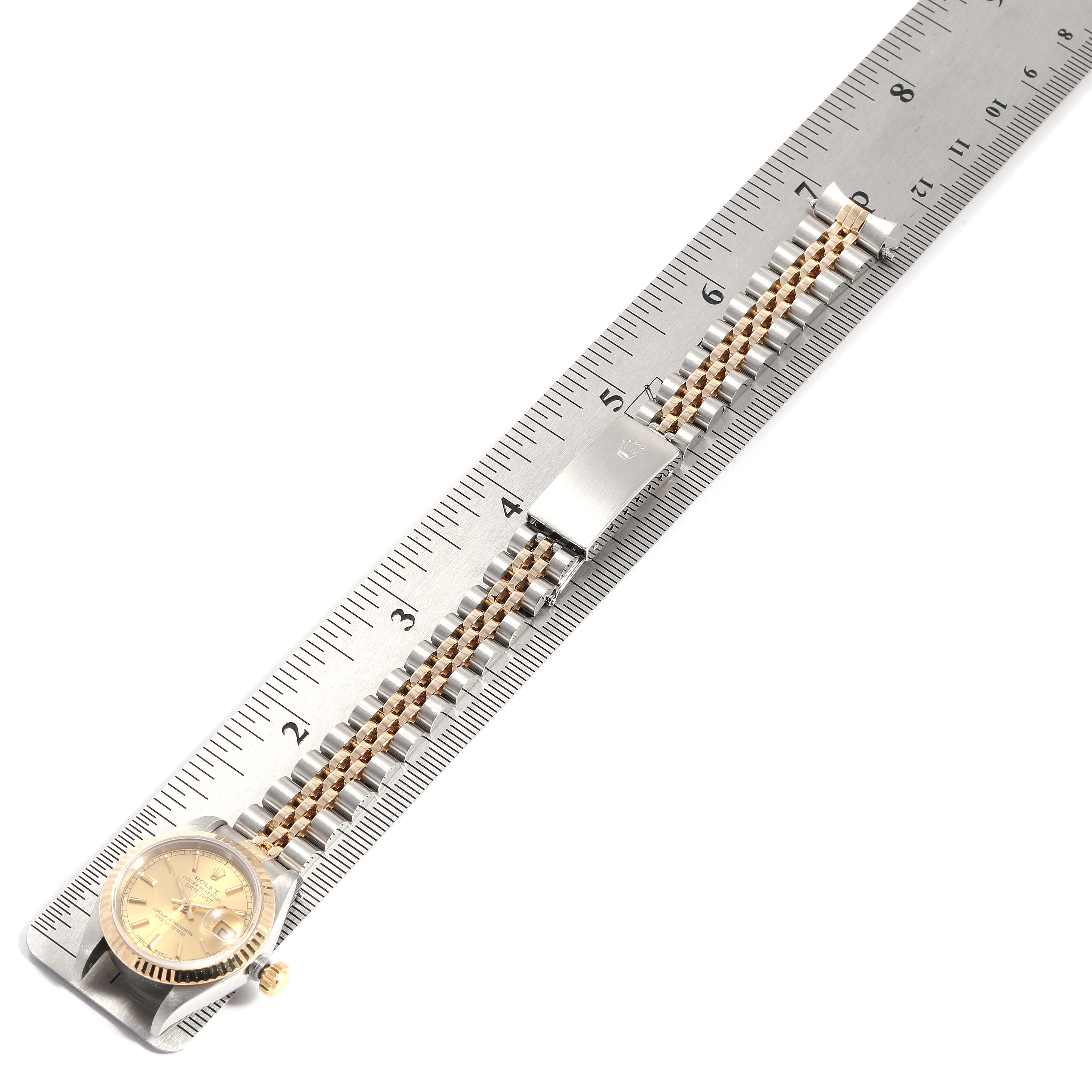 The image shows the Rolex Datejust 69173 Women
s Steel and Gold (two tone) Champagne Dial 69173 Women
s Steel and Gold (two tone) Champagne Dial watch with a ruler, displaying the face and the metal bracelet.