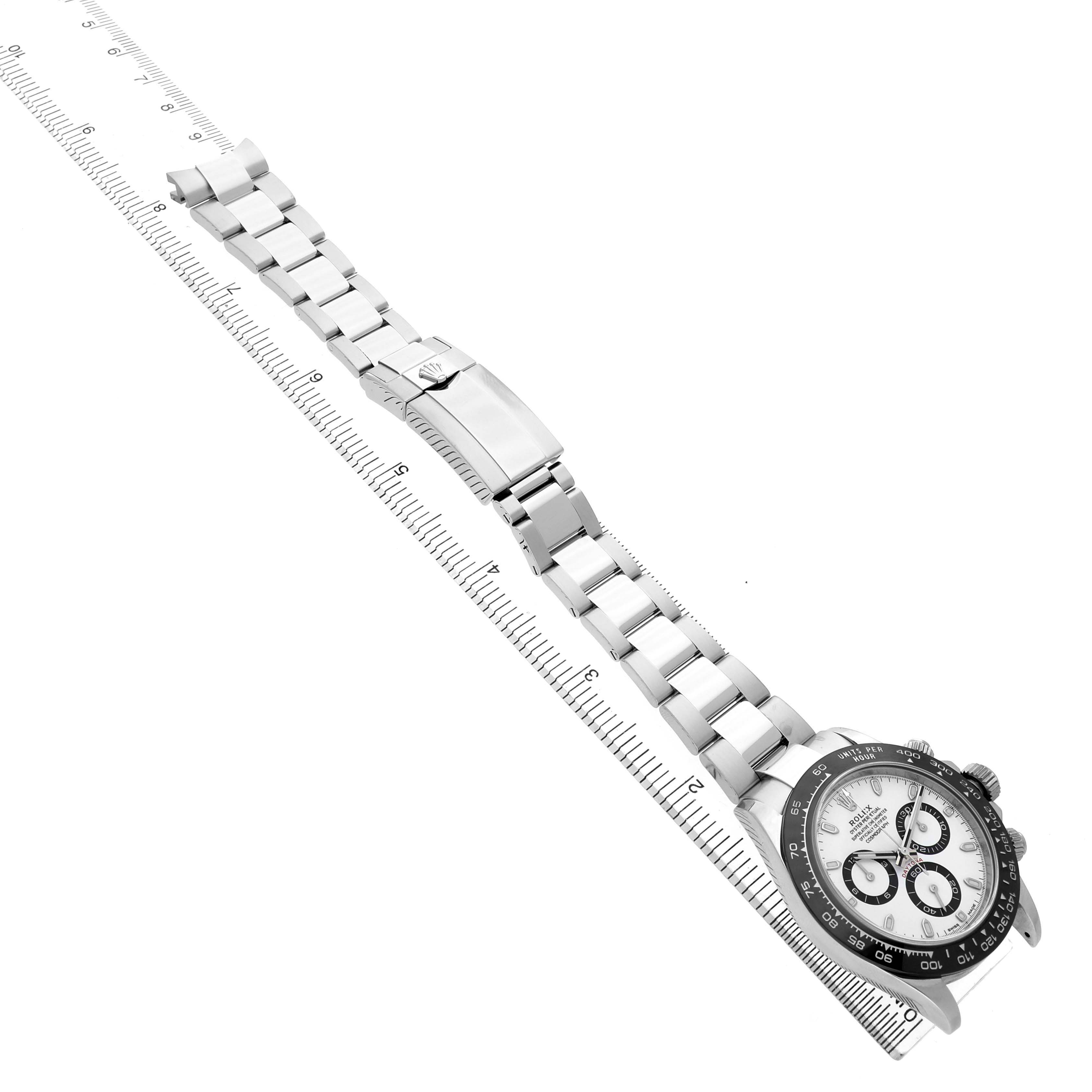 The Rolex Daytona 116500LN Men's Stainless Steel White Dial is shown at a slight angle displaying the full bracelet, clasp, and face against a measurement grid.