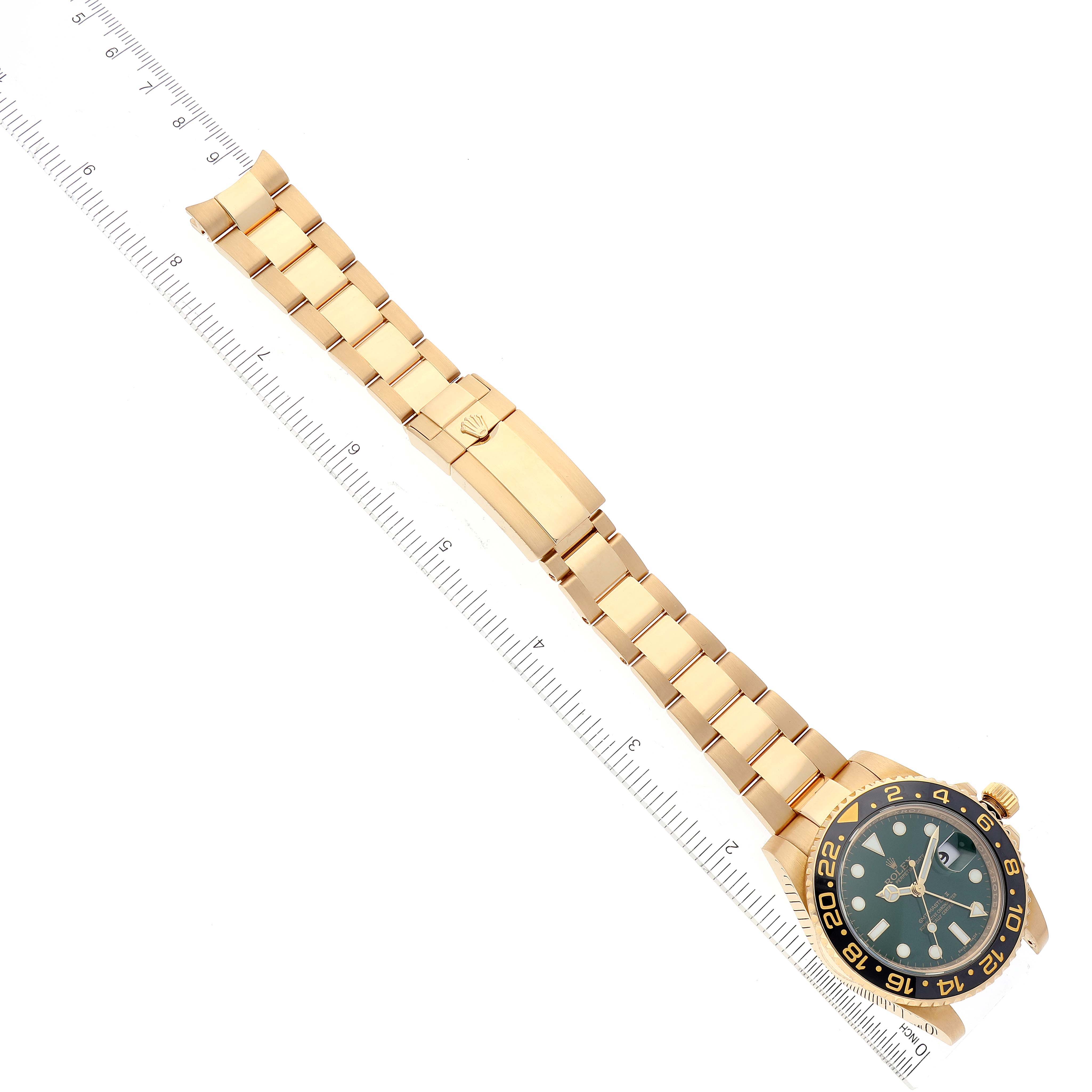 This image shows a Rolex GMT-Master 116718 Men's Yellow Gold Green Dial 116718 Men's Yellow Gold Green Dial watch laid flat with the bracelet fully extended next to a ruler for scale.