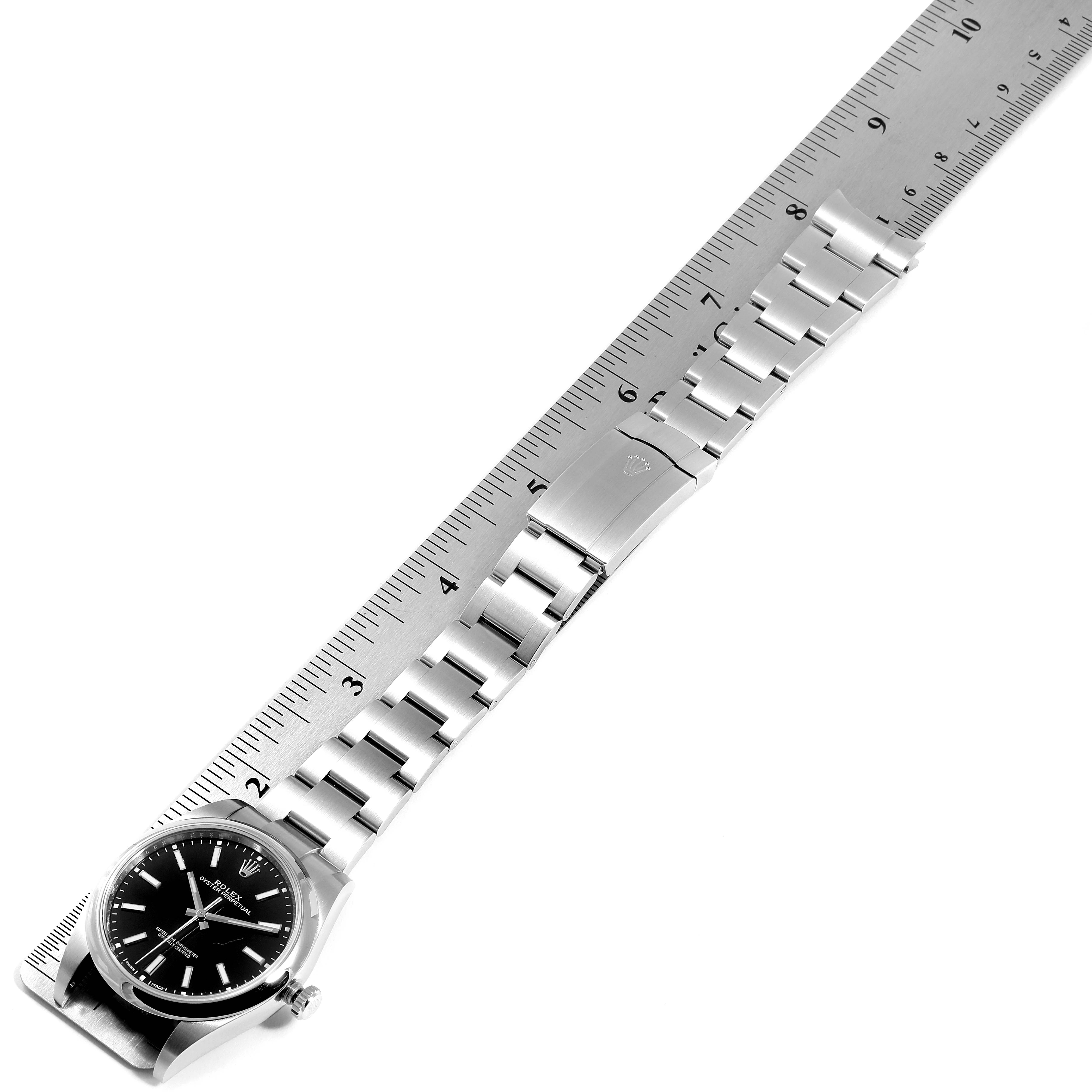 The image shows the Rolex Oyster Perpetual 114300 Men's Stainless Steel Black Dial 114300 Men's Stainless Steel Black Dial watch, focusing on its face and metal bracelet, positioned alongside a ruler for measurement.