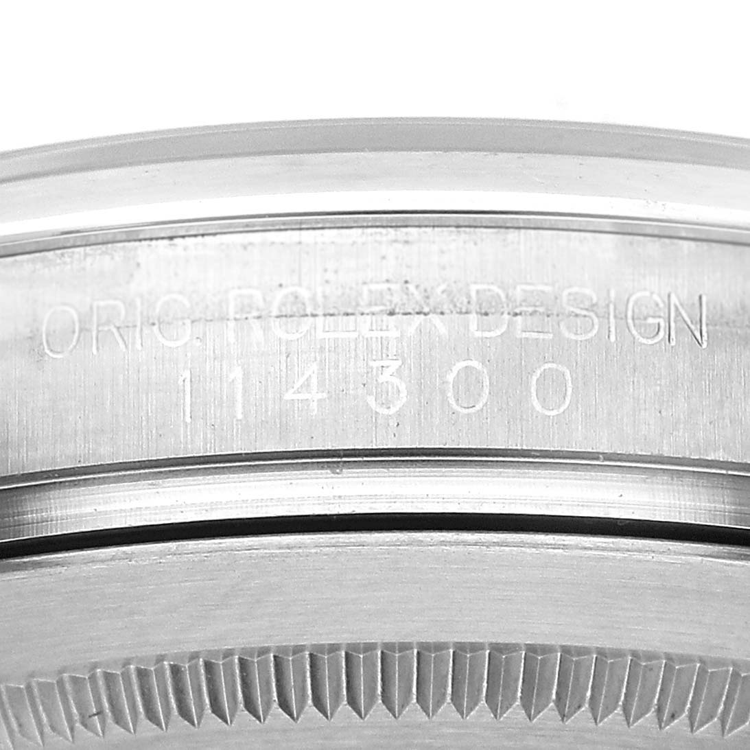 The image shows a close-up of the side engraving on the bezel of a Rolex Oyster Perpetual 114300 Men's Stainless Steel Grey Dial watch.