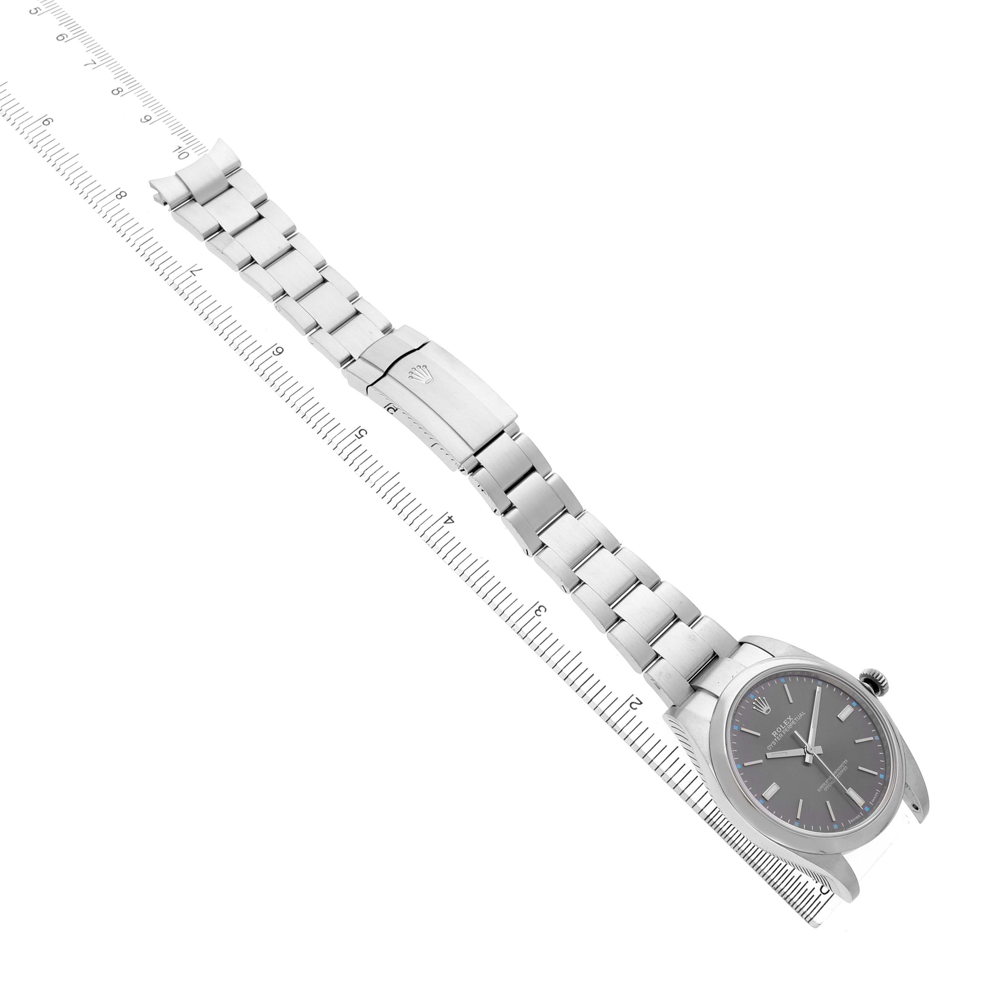 The image shows a Rolex Oyster Perpetual 114300 Men's Stainless Steel Grey Dial watch laid flat with its face, bracelet, and clasp visible on a measuring guide.