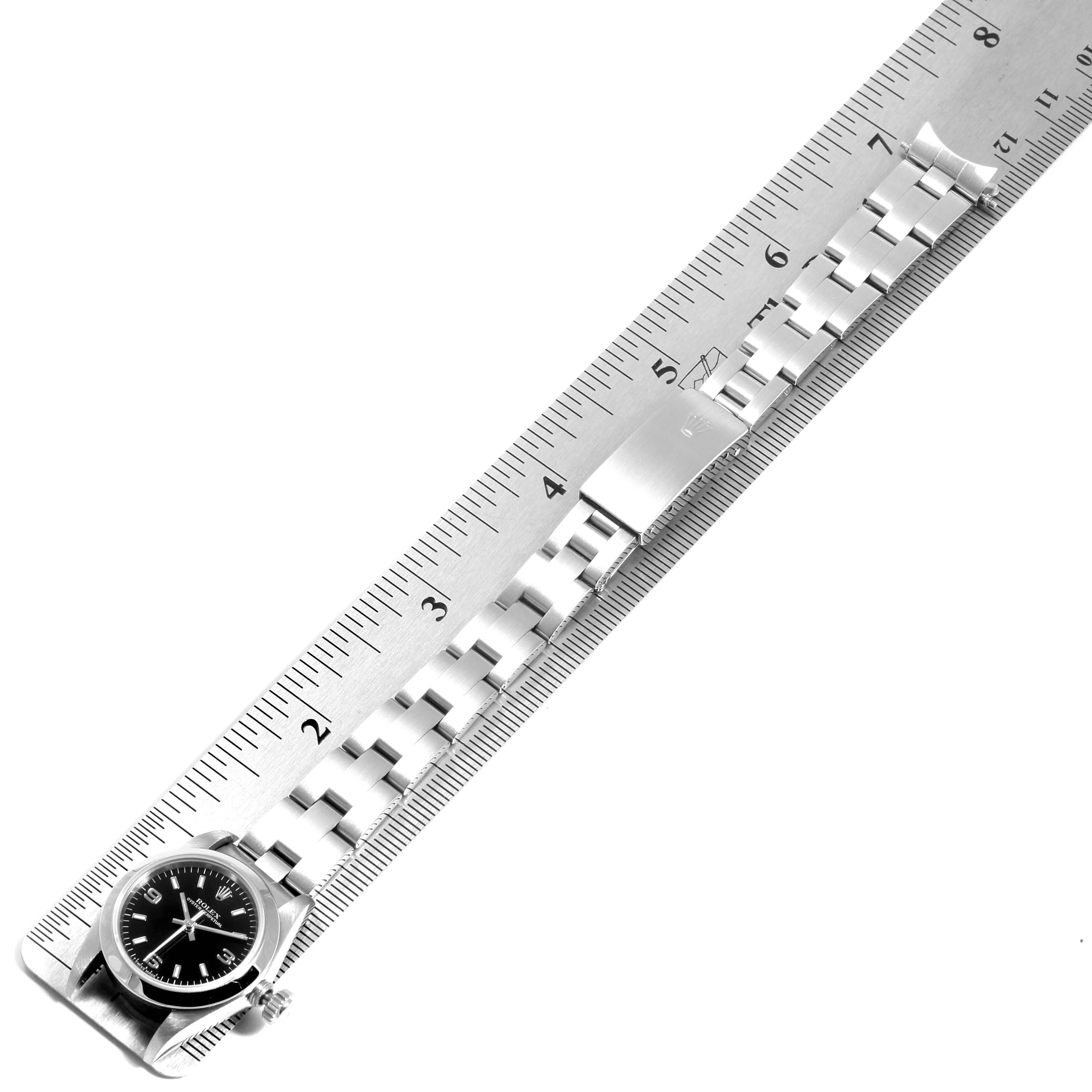 The image shows the face and bracelet of a Rolex Oyster Perpetual 67180 Women
s Stainless Steel Black Dial 67180 Women
s Stainless Steel Black Dial watch placed along a ruler for measurement.