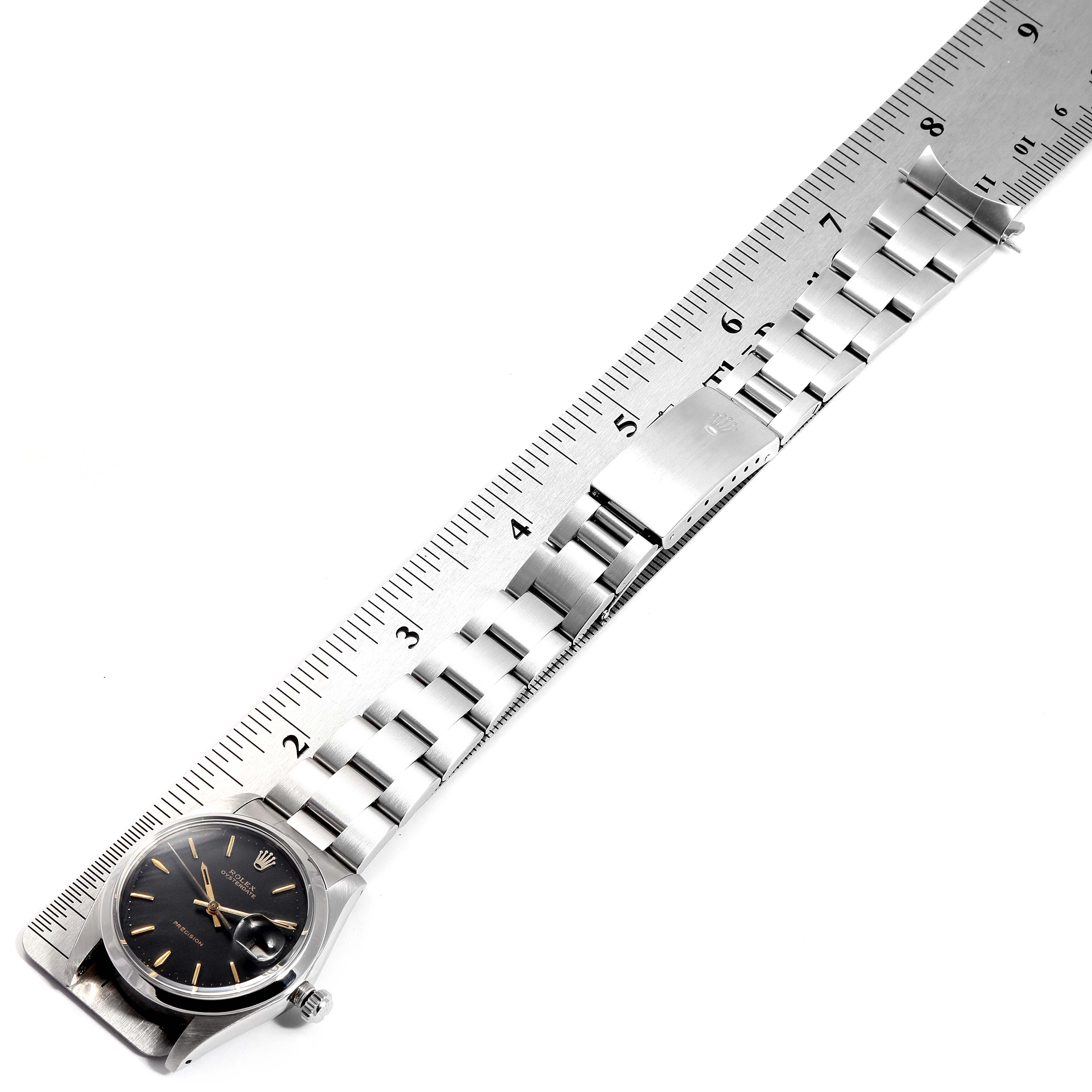 The image shows a Rolex Vintage Collection 6694 Men
s Stainless Steel Black Dial 6694 Men
s Stainless Steel Black Dial watch with a stainless steel bracelet and clasp, alongside a measuring ruler.