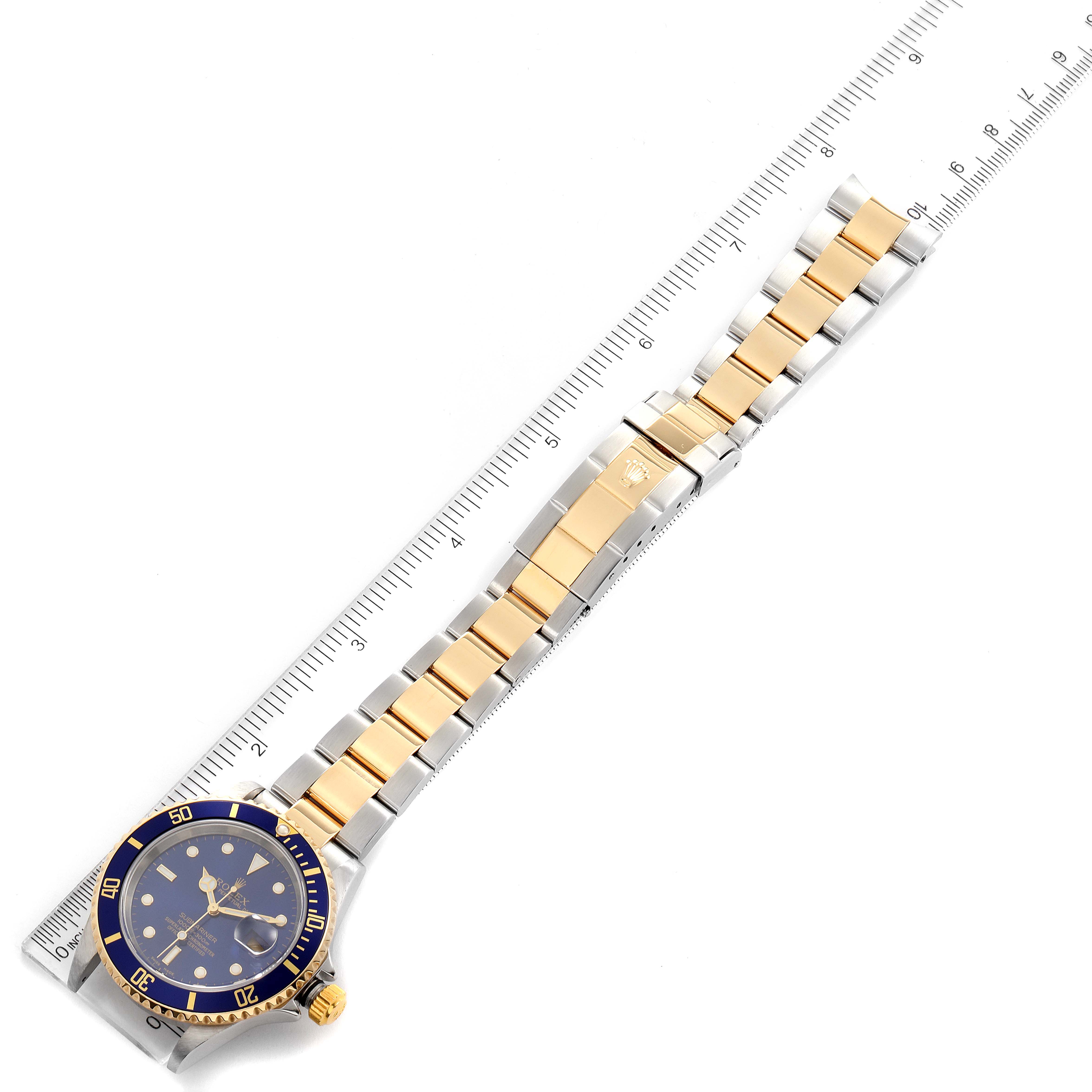 The image shows the entire Rolex Submariner 16613 Men
s Steel and Gold (two tone) Blue Dial 16613 Men
s Steel and Gold (two tone) Blue Dial watch with a focus on the band, laid next to a ruler for scale.