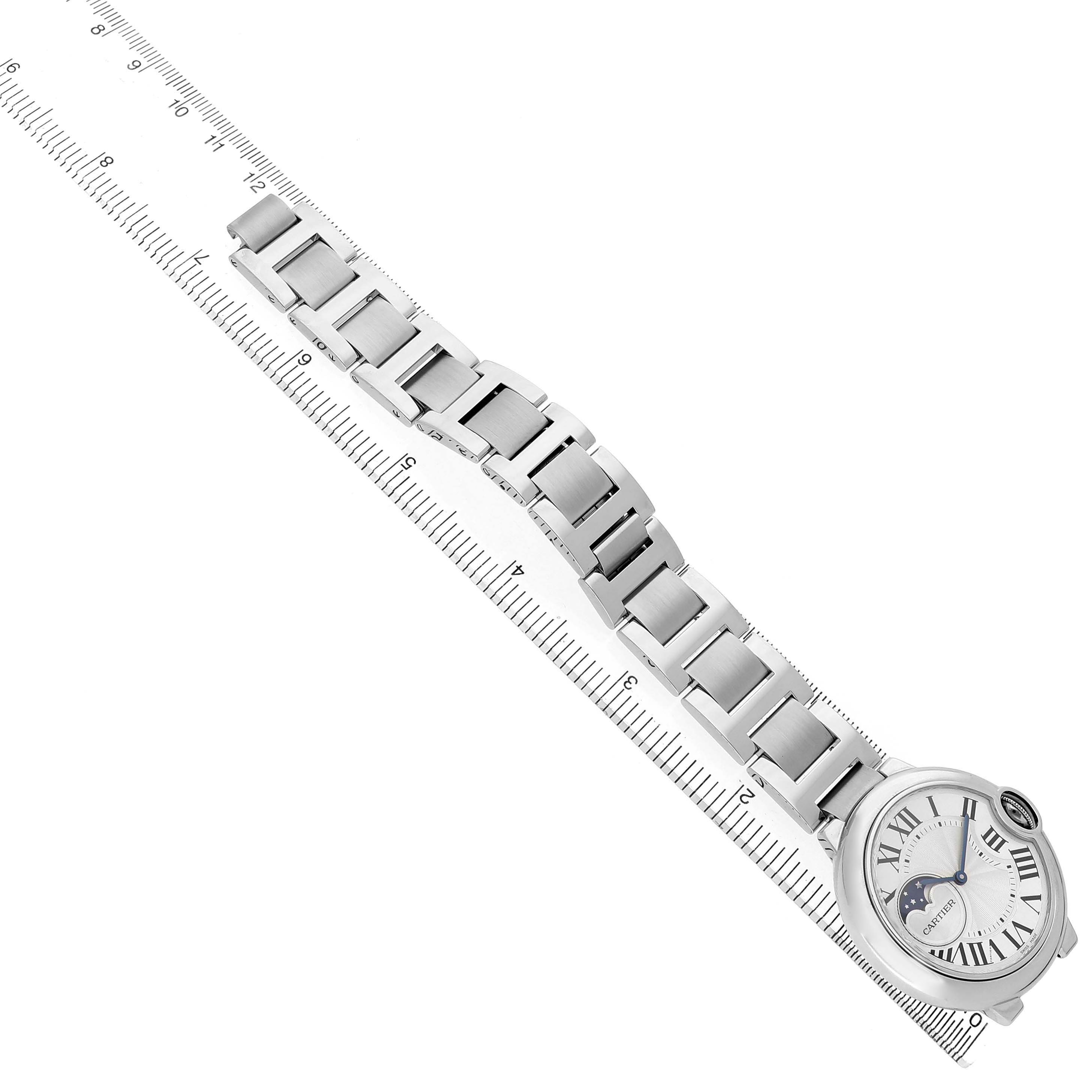 The Cartier Ballon Bleu WSBB0021 Men's Stainless Steel Silver Dial watch is shown from an overhead angle, displaying its face and full metal bracelet alongside a ruler.
