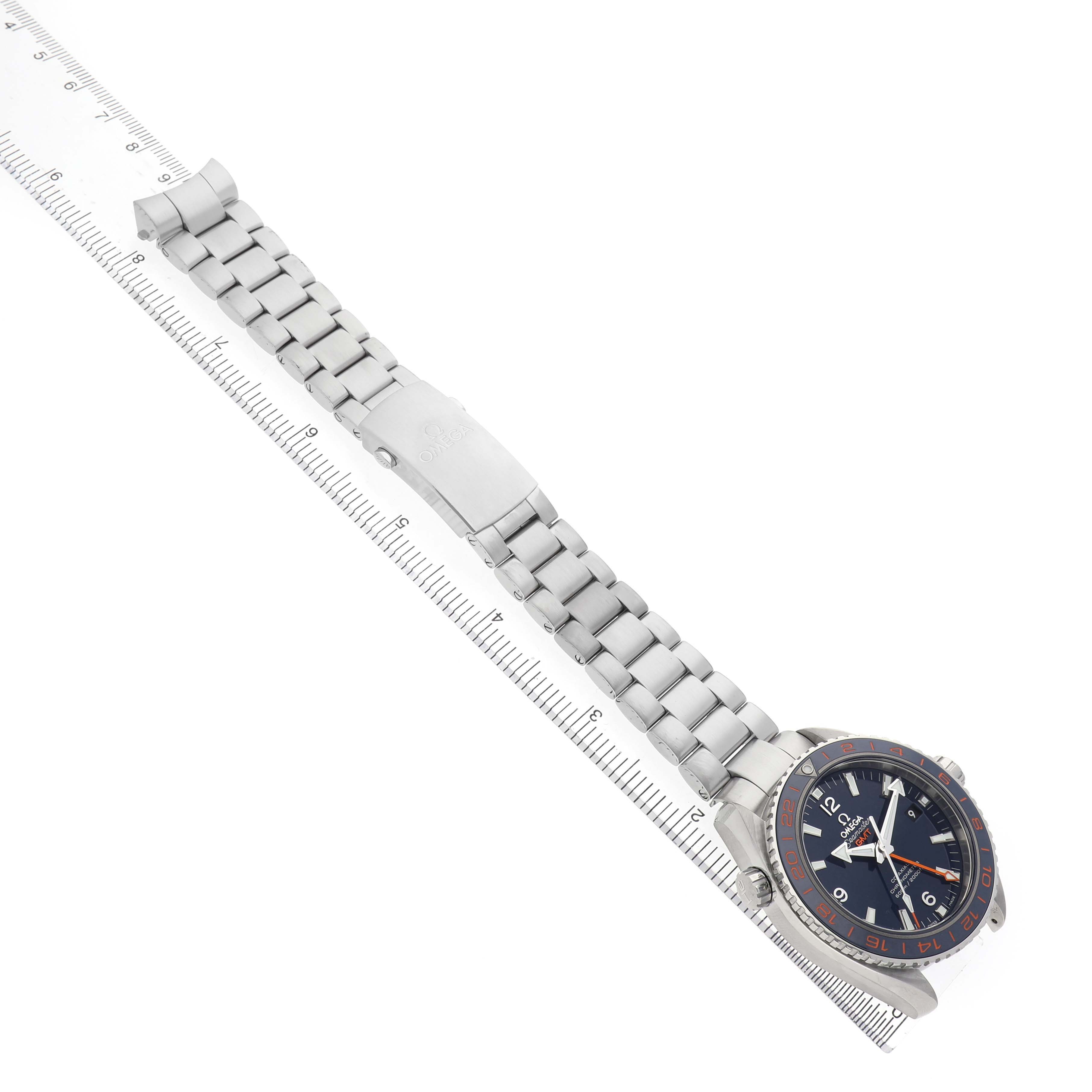 The Omega Planet Ocean 232.30.44.22.03.001 Men's Stainless Steel Blue Dial watch is shown at an angle displaying the face, bezel, and full metal bracelet alongside a ruler.