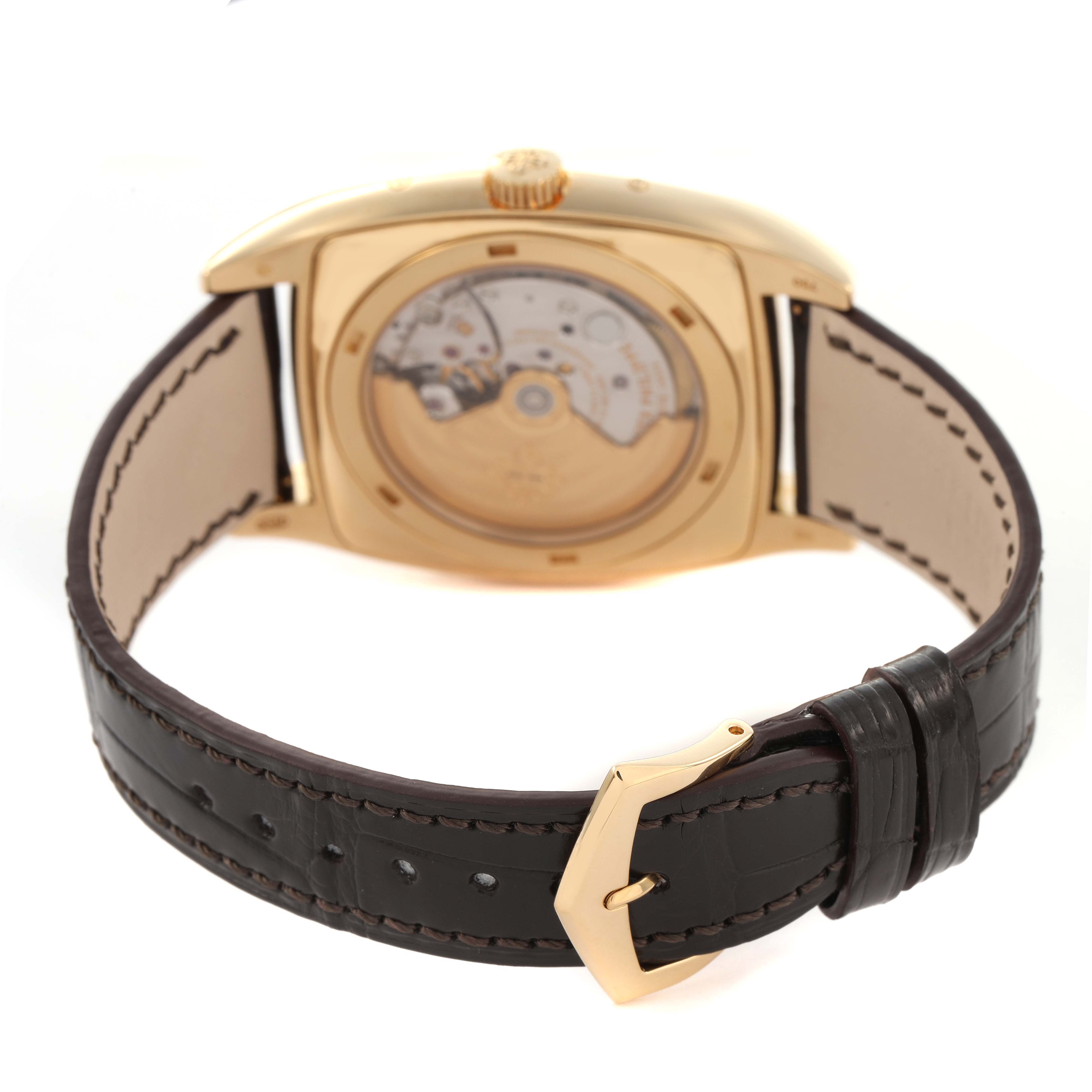 The Patek Philippe Gondolo 5135J-001 Men's Yellow Gold Silver Dial watch is shown from the back, highlighting its transparent case back and leather strap.