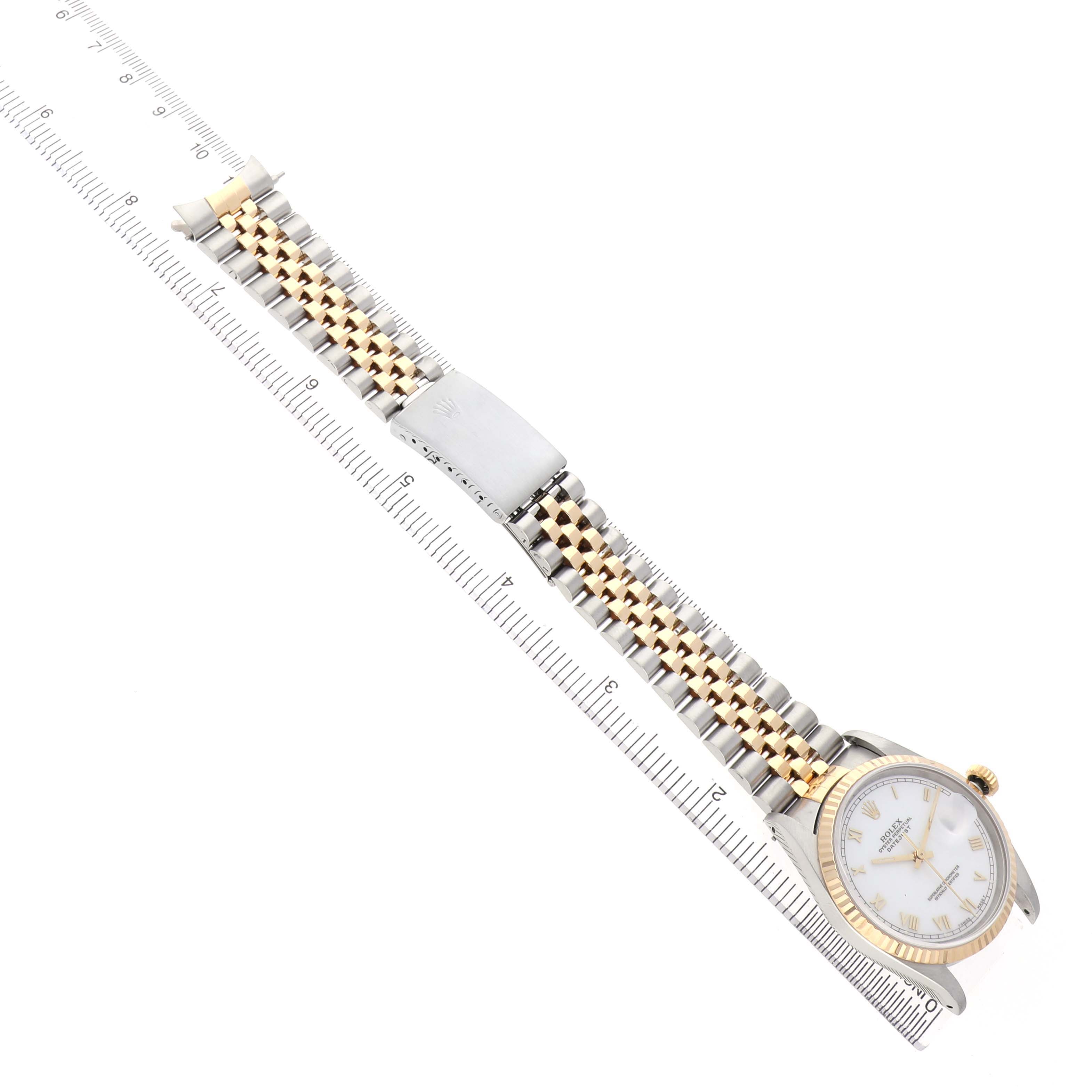 The Rolex Datejust 16233 Men's Steel and Gold (two tone) White Dial watch is shown from a top angle, displaying the face, bracelet, and clasp, alongside a measuring ruler.