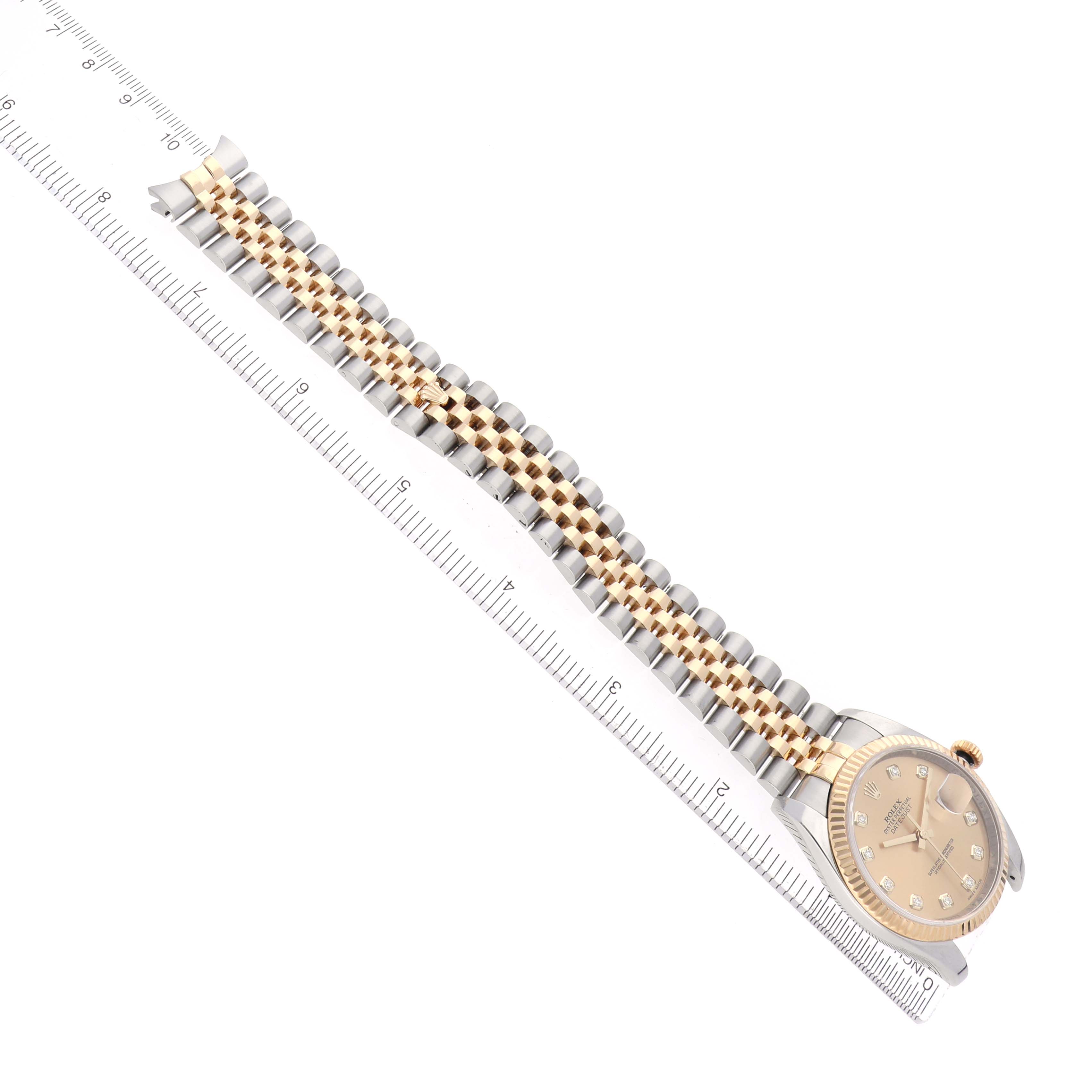 The Rolex Datejust model 116233 is shown at an angled view, depicting the full watch with its champagne-colored dial and two-tone jubilee bracelet aligned with a ruler.