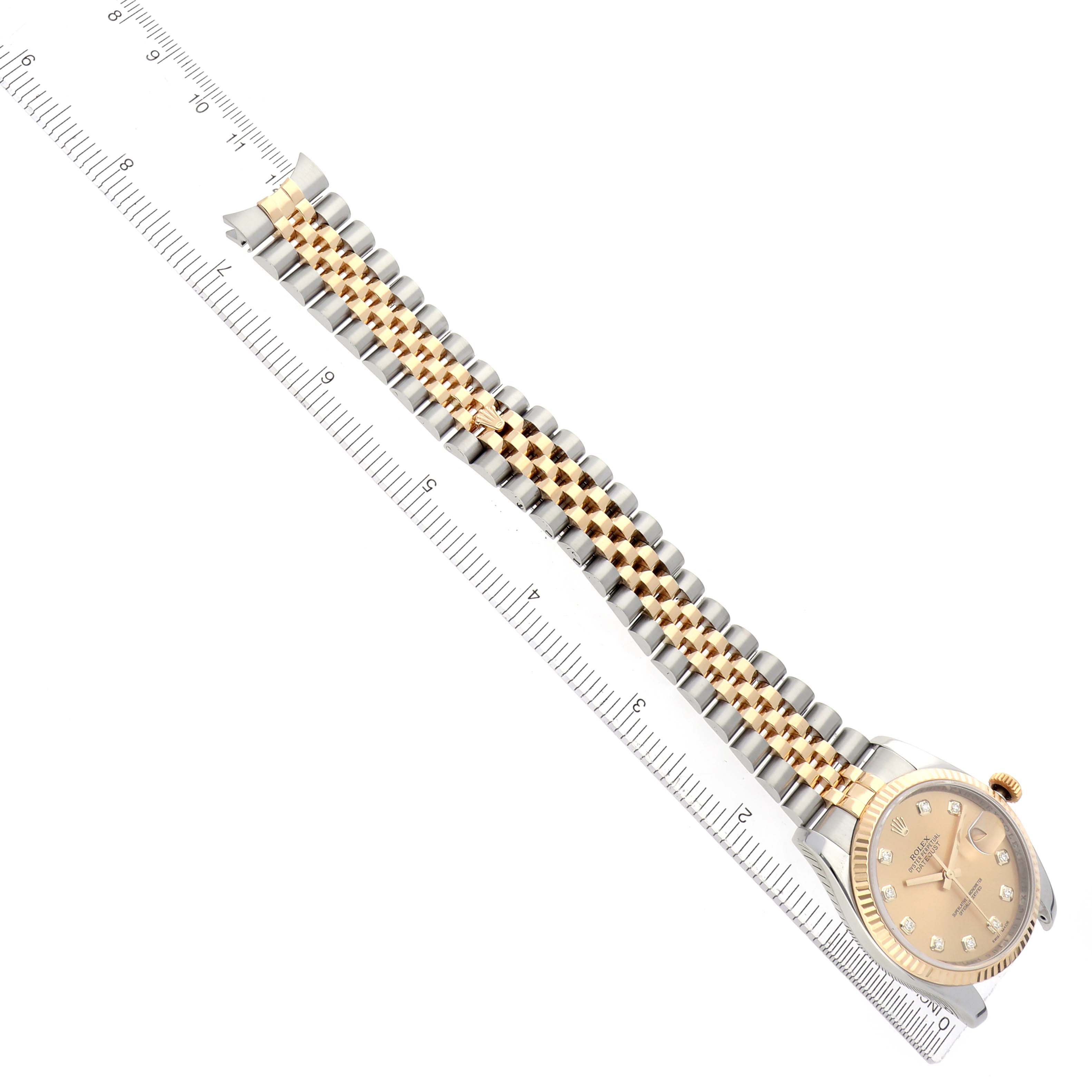 The Rolex Datejust model 116233 is shown at an angle displaying the gold dial, fluted bezel, and two-tone bracelet alongside a measuring ruler.