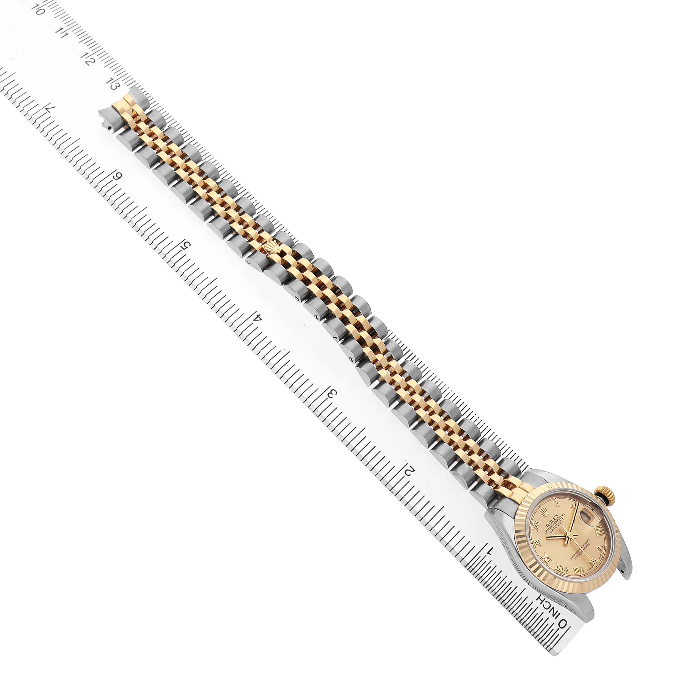The Rolex Datejust 179173 Women's Steel and Gold (two tone) Champagne Dial watch is shown at an angle, highlighting the face and entire two-tone bracelet alongside a ruler.
