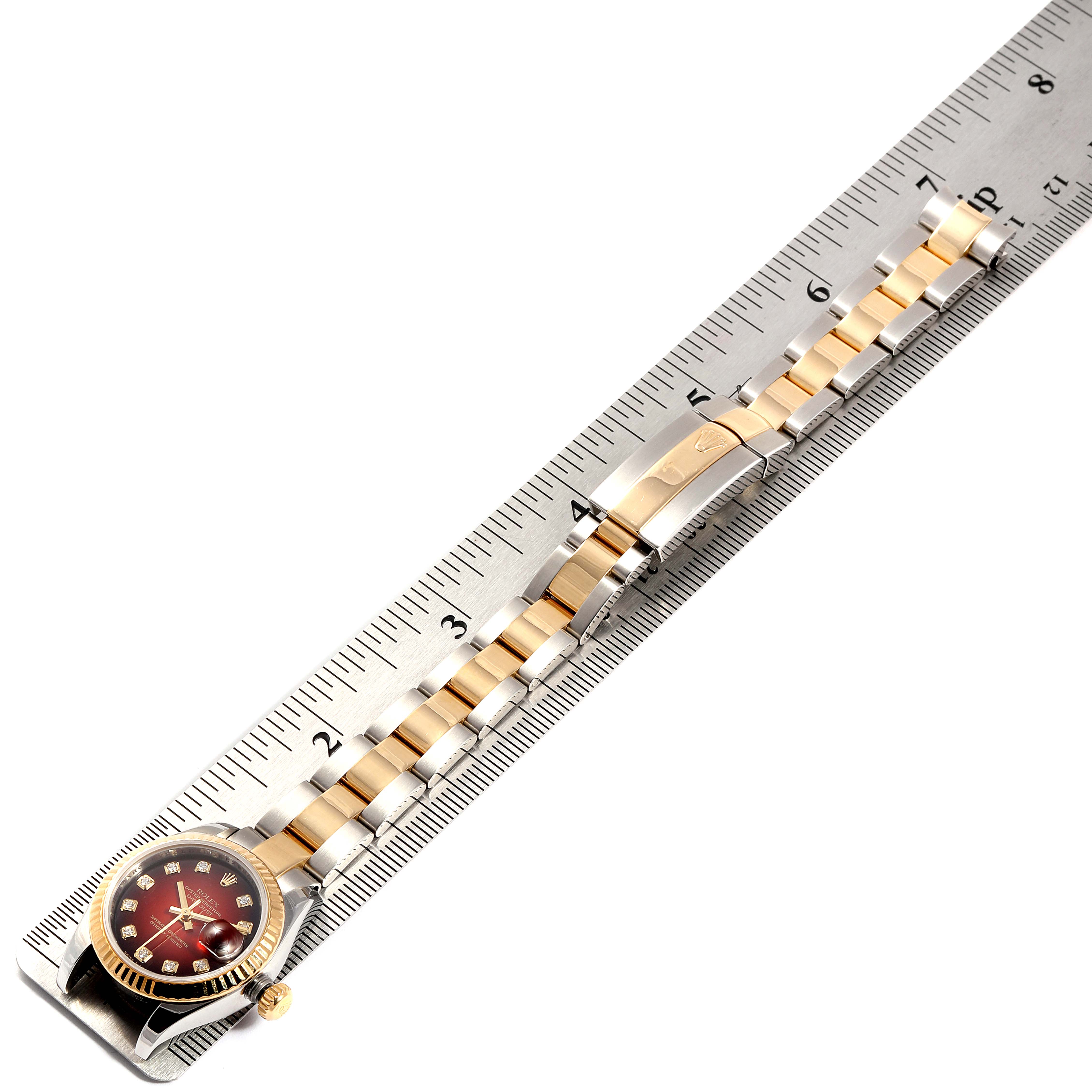 The Rolex Datejust 179173 Women's Steel and Gold (two tone) Red Dial 179173 Women's Steel and Gold (two tone) Red Dial is displayed flat on a ruler, showing the face, bezel, band, and clasp in a horizontal position.