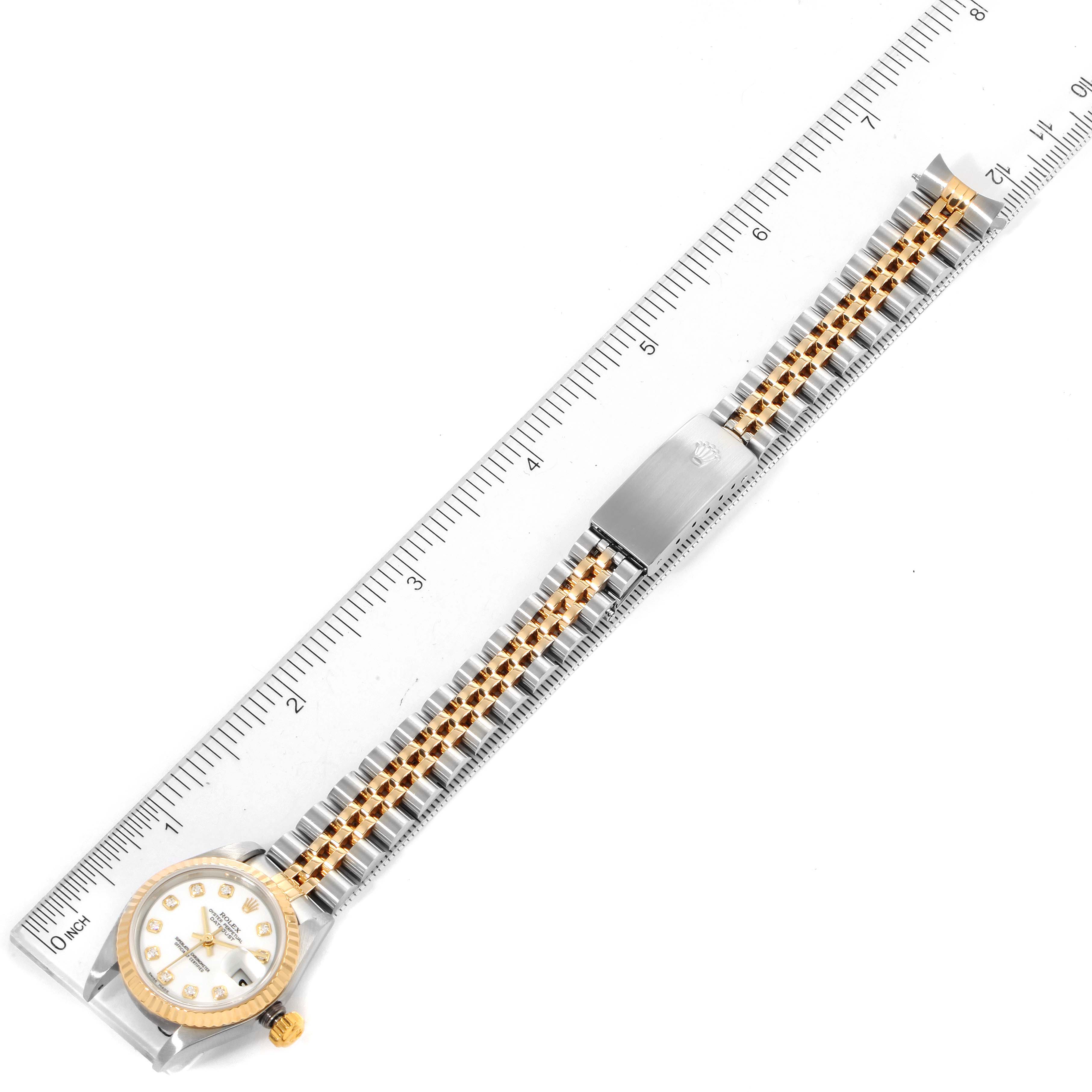 This image shows a Rolex Datejust 79173 Women
s Steel and Gold (two tone) White Dial 79173 Women
s Steel and Gold (two tone) White Dial watch laid flat, with a ruler alongside its gold and silver bracelet.