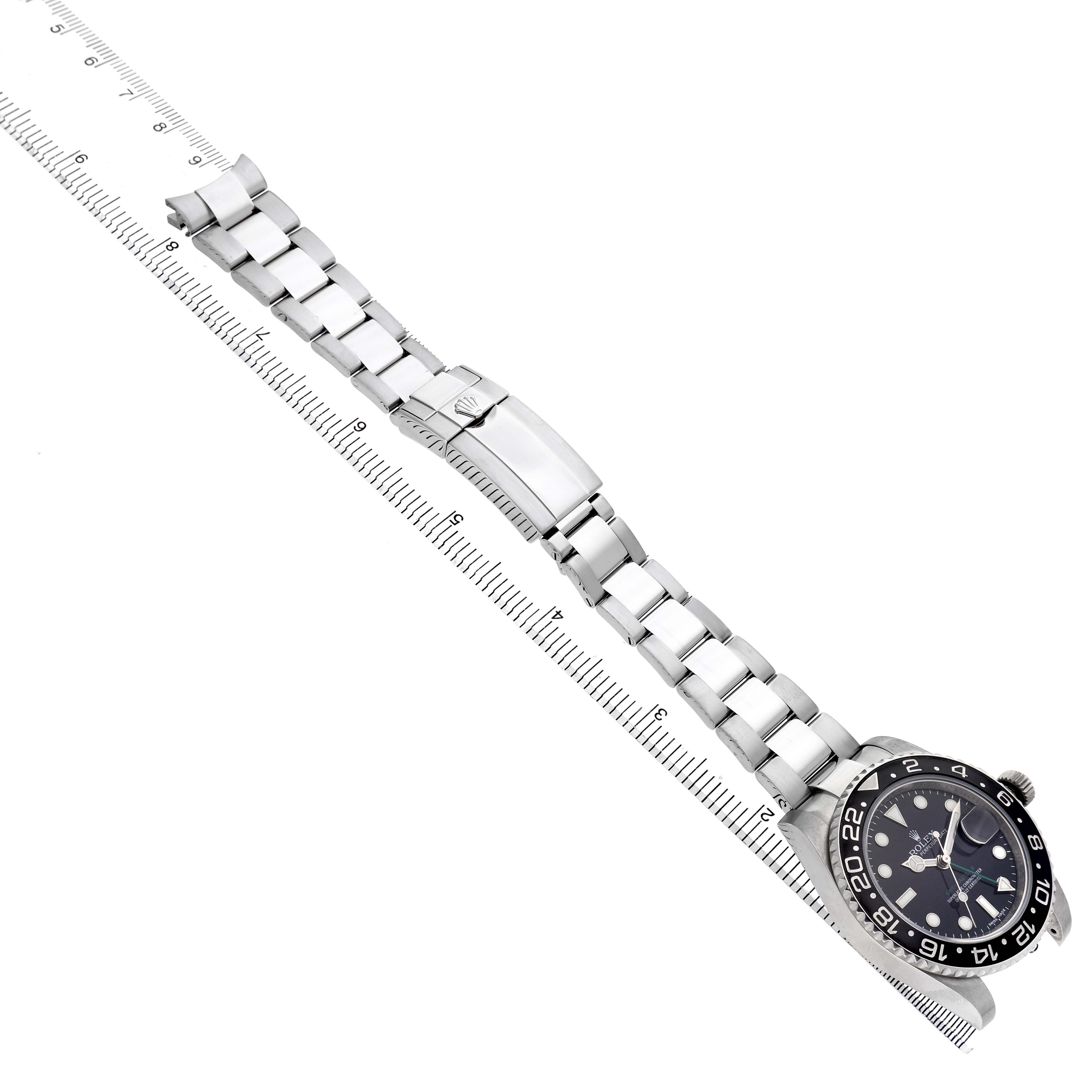 The Rolex GMT-Master 116710 Men's Stainless Steel Black Dial watch is shown from an elevated angle, featuring the watch face, bezel, and full metal bracelet alongside a ruler.