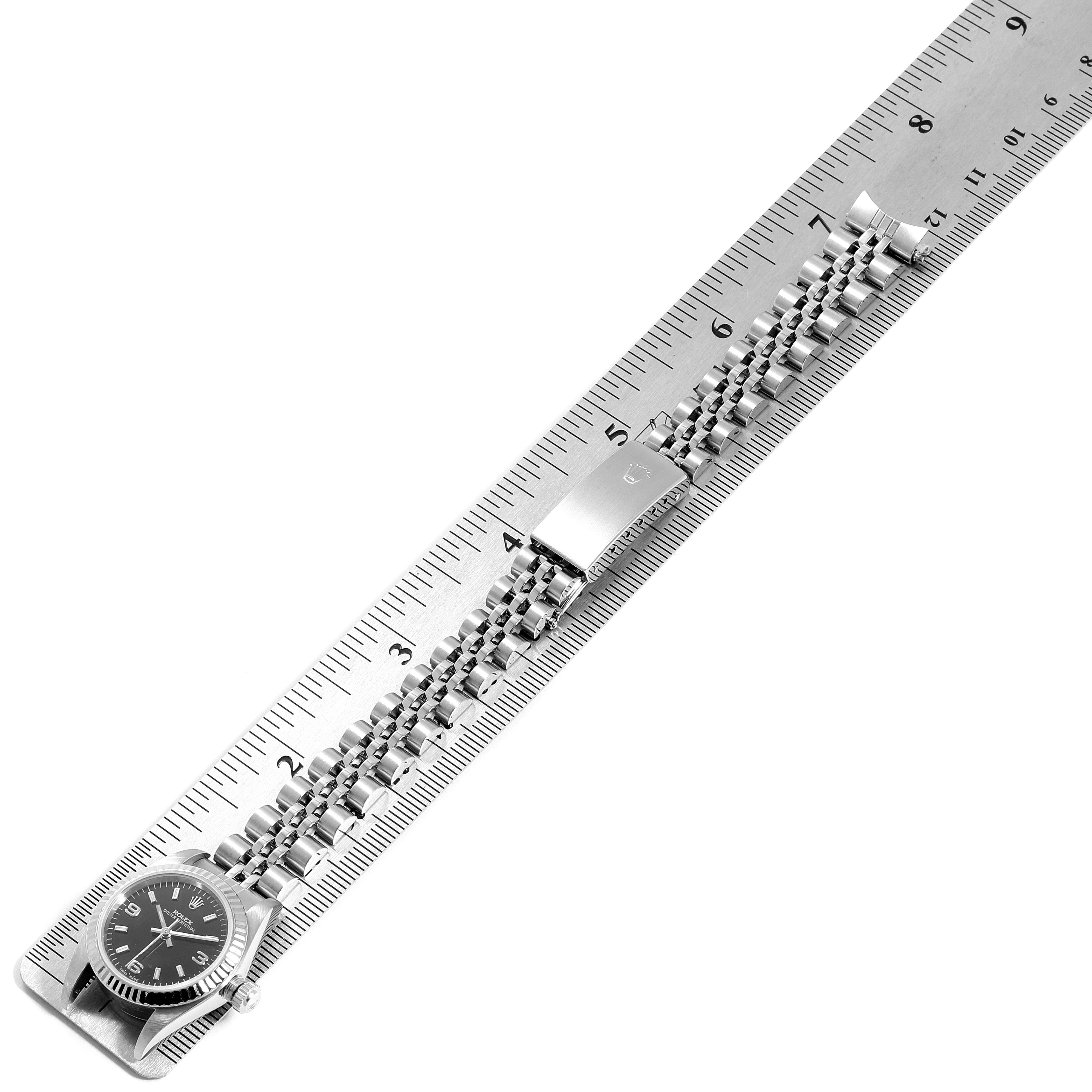 The image shows the entire length of a Rolex Oyster Perpetual 76094 Women
s Stainless Steel Black Dial 76094 Women
s Stainless Steel Black Dial watch, including its dial, case, and bracelet, placed against a ruler.