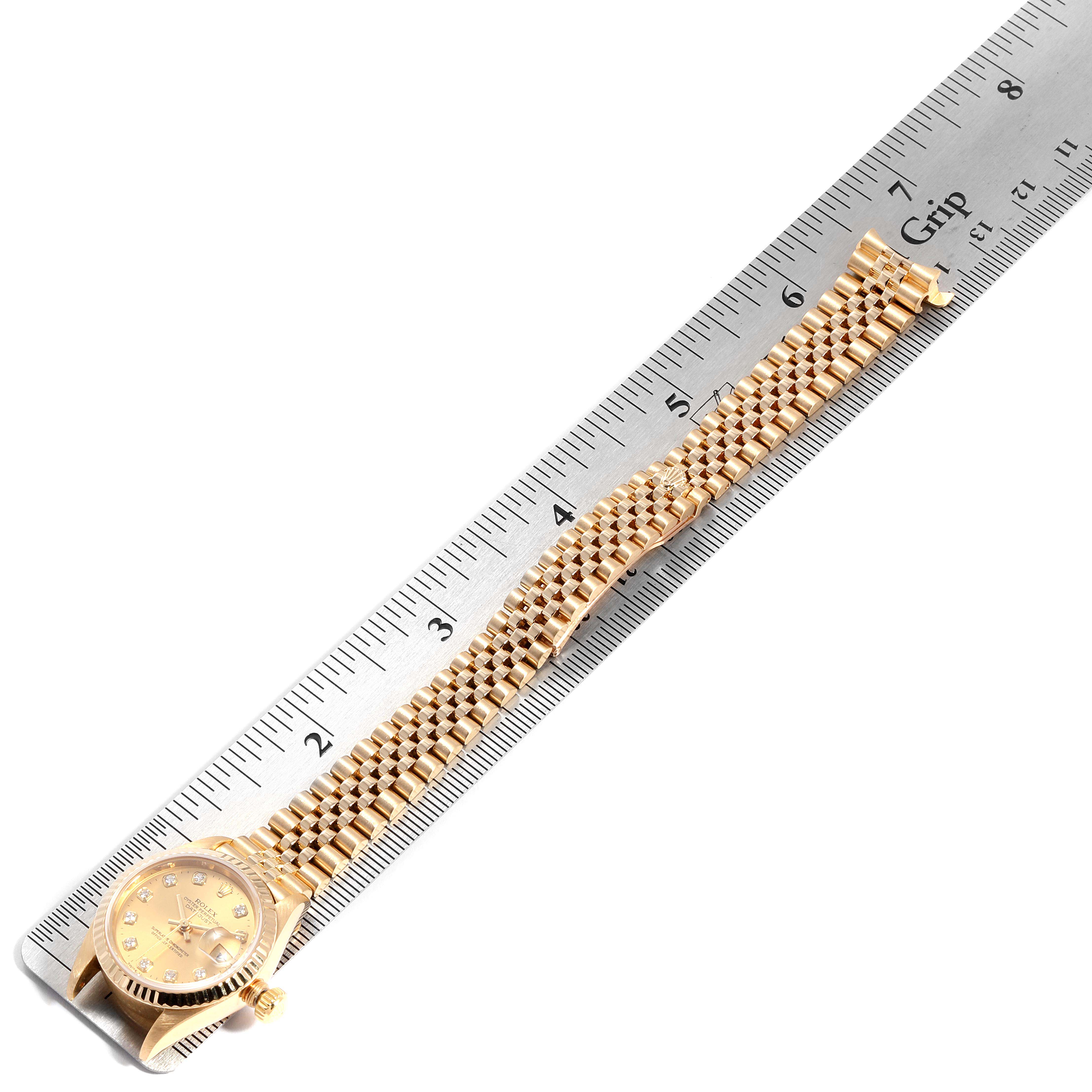 The image shows a Rolex President 79178 Women
s Yellow Gold Champagne Dial 79178 Women
s Yellow Gold Champagne Dial model watch laid flat next to a ruler, displaying its face, bracelet, and clasp.